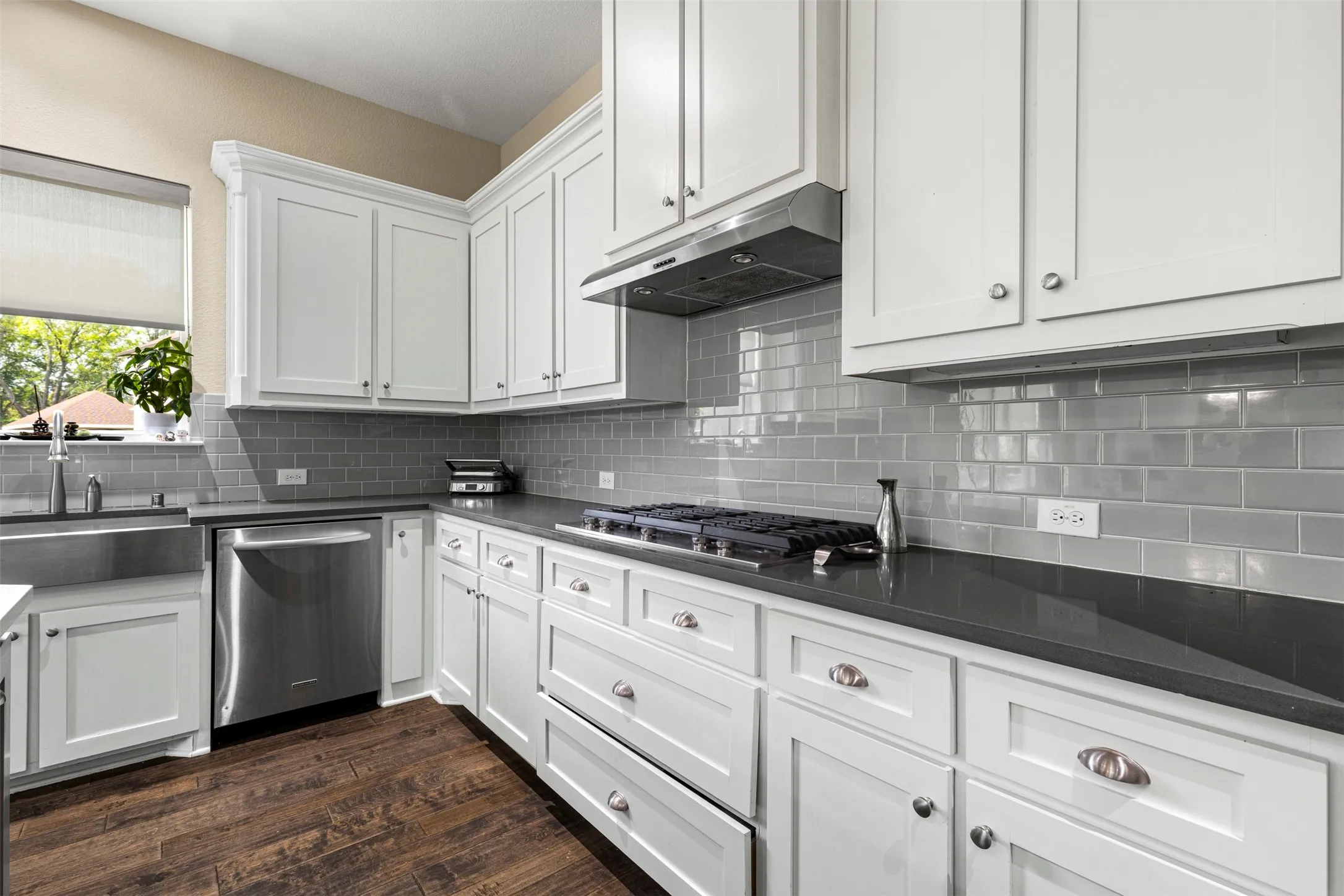 Kitchen featuring white shaker-style cabinetry, dark stone countertops, stainless steel appliances, subway tile backsplash, and wood-finish flooring