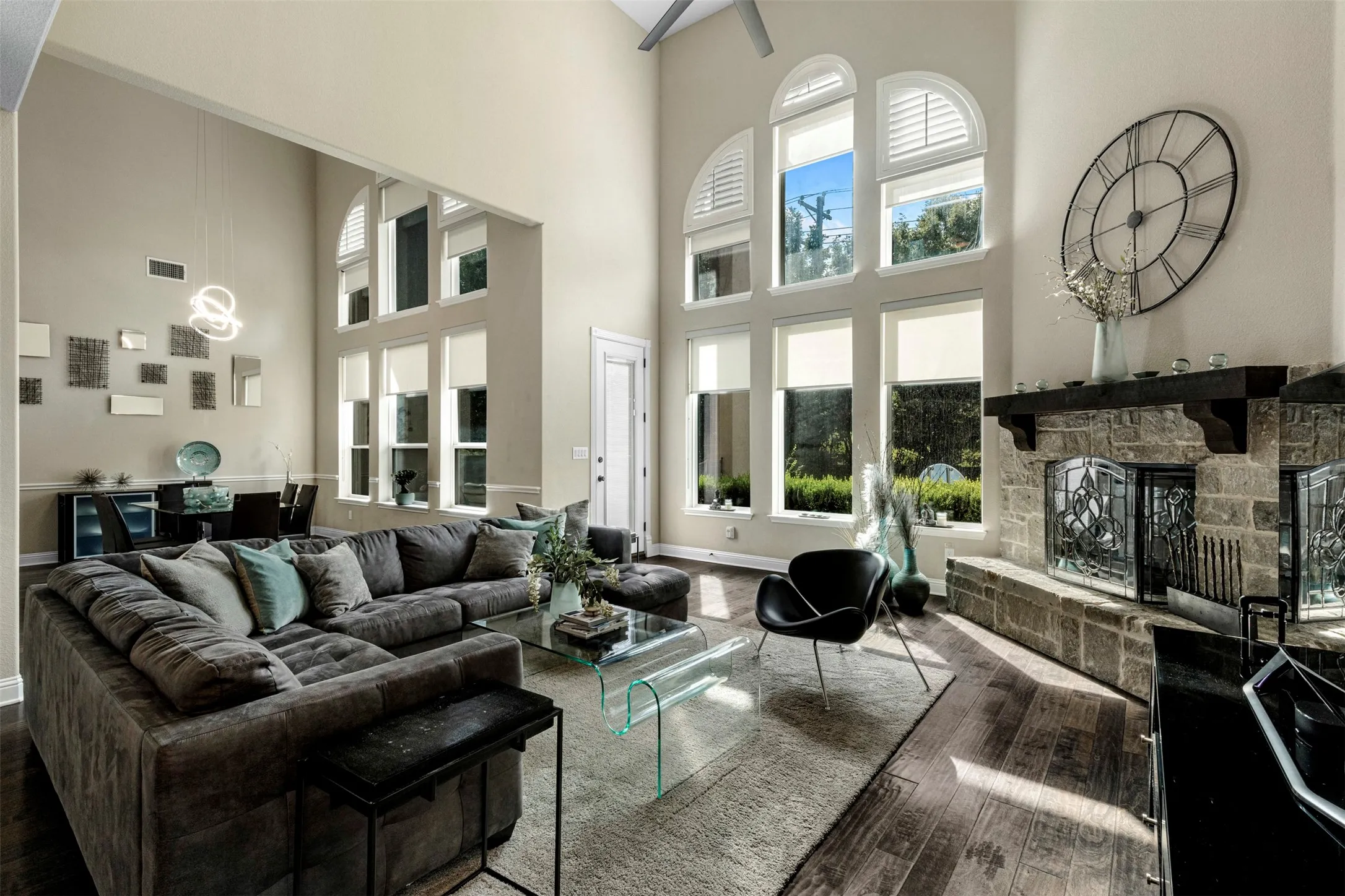 Two-story vaulted ceiling with expansive arched windows, stone-surround fireplace with a dark timber mantel, and wood-finish flooring