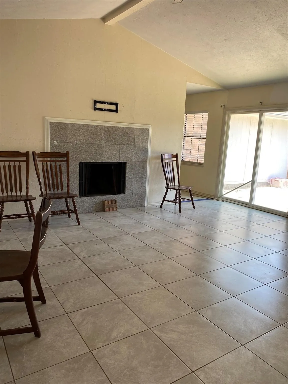 Vaulted ceiling, stone-surround fireplace, large-format tile flooring, and sliding glass doors