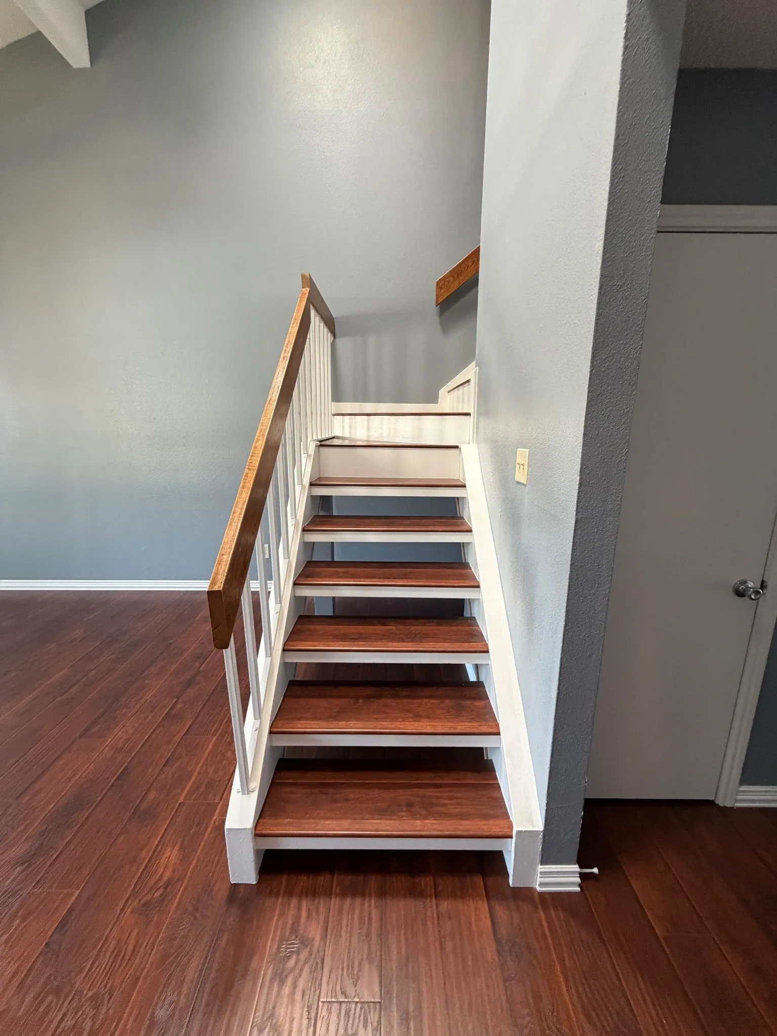 Staircase featuring wood-finish treads, white balusters, and a natural wood handrail, set against wood-finish flooring and high vaulted ceilings