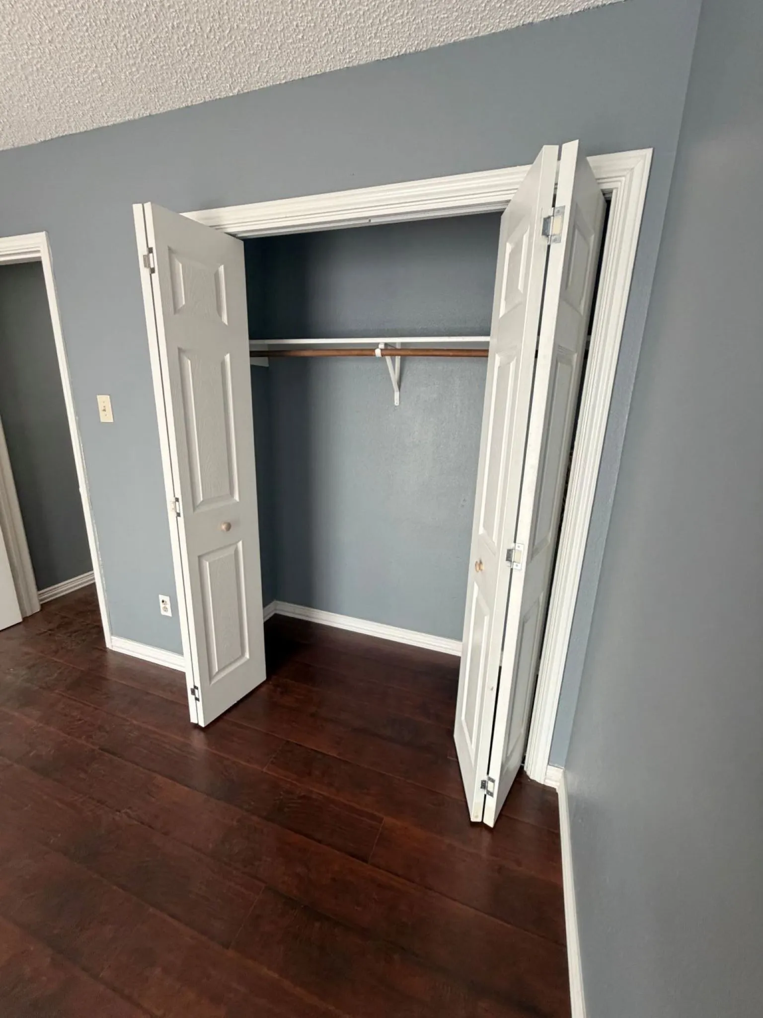 Closet featuring white six-panel bifold doors and a built-in hanging rod, complemented by dark wood-finish flooring