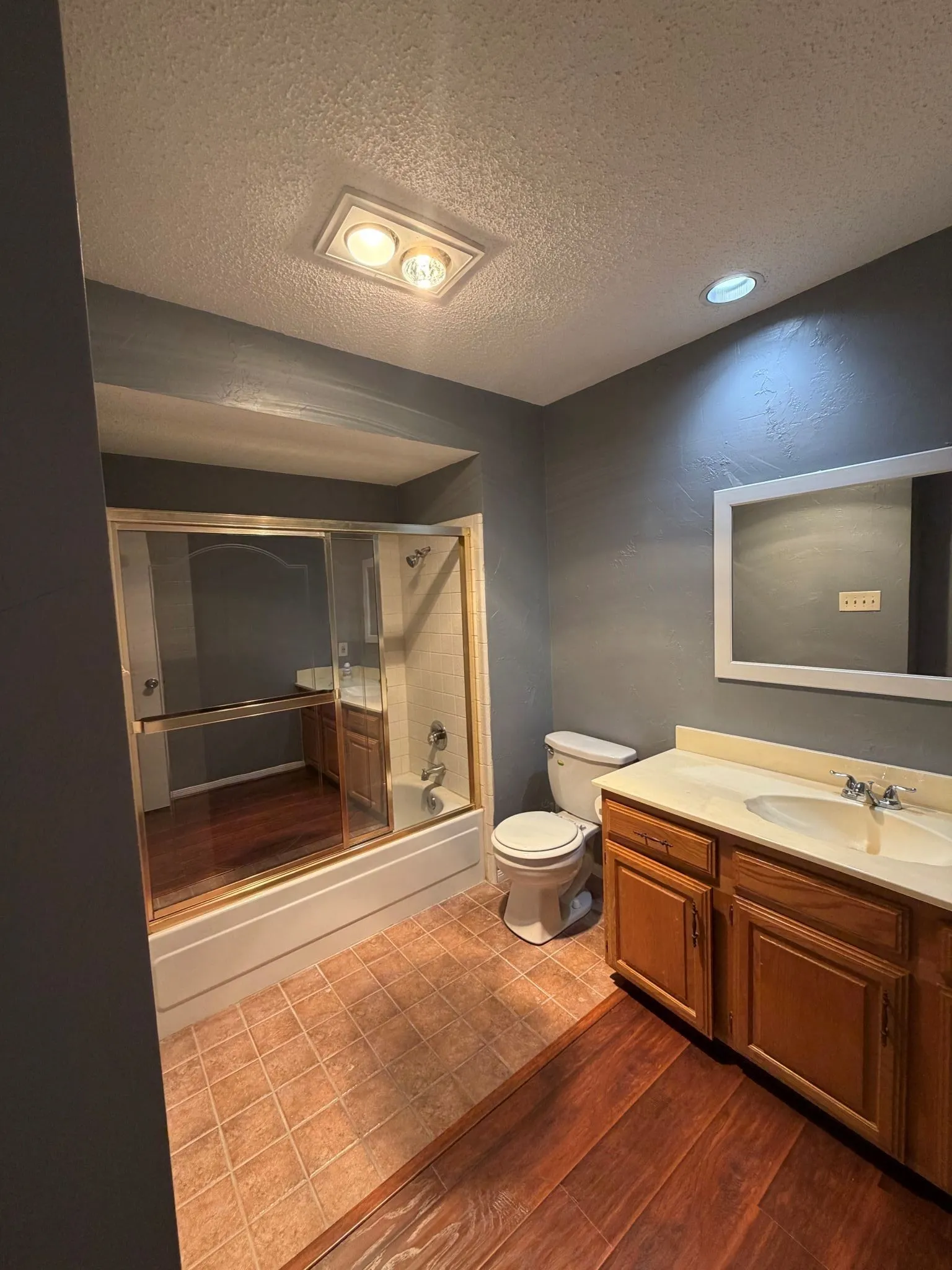 Bathroom featuring wood-finish cabinetry, a white countertop with an integrated sink, a built-in tub with a sliding glass enclosure, and a wall-mounted mirror