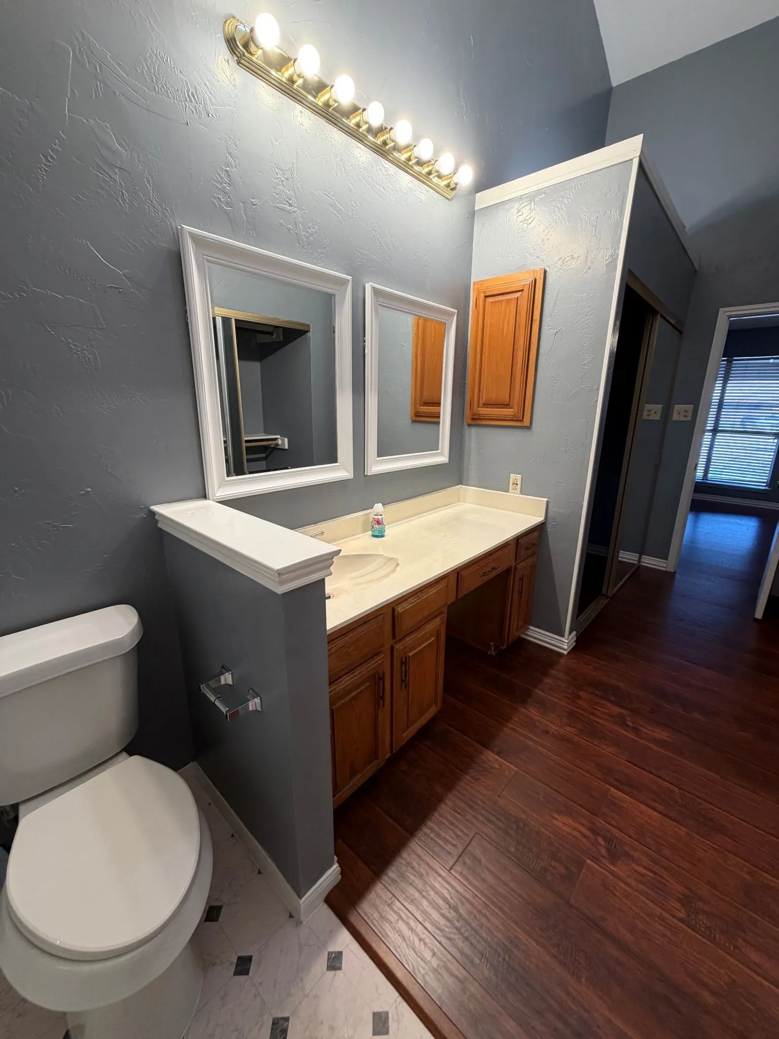 Bathroom vanity featuring wood-finish cabinetry, a solid surface countertop, an integrated sink, dual wall-mounted mirrors, and an eight-bulb overhead fixture