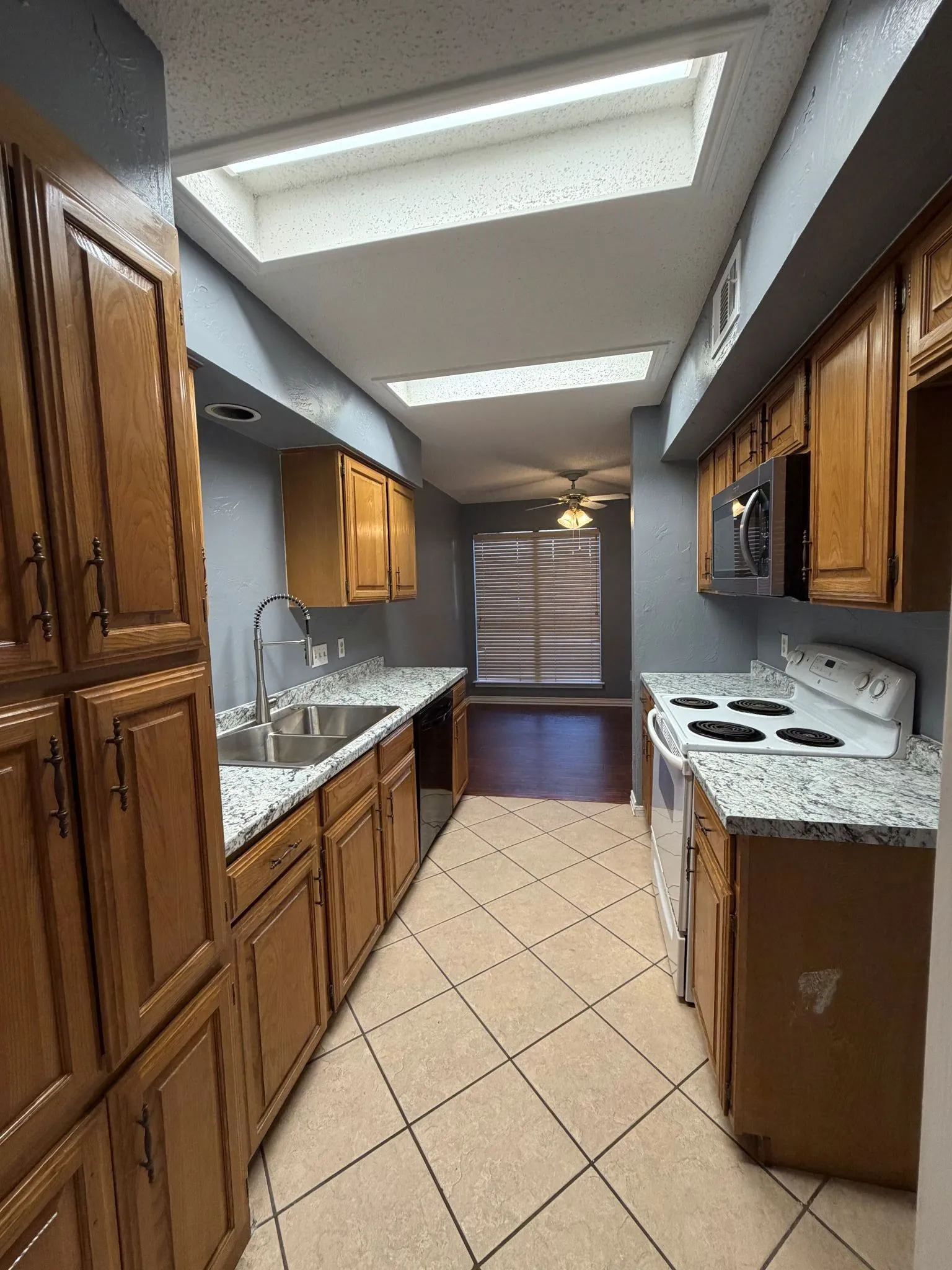 Kitchen featuring natural wood cabinetry, stone-patterned countertops, dual skylights, tile flooring, and stainless steel integrated appliances