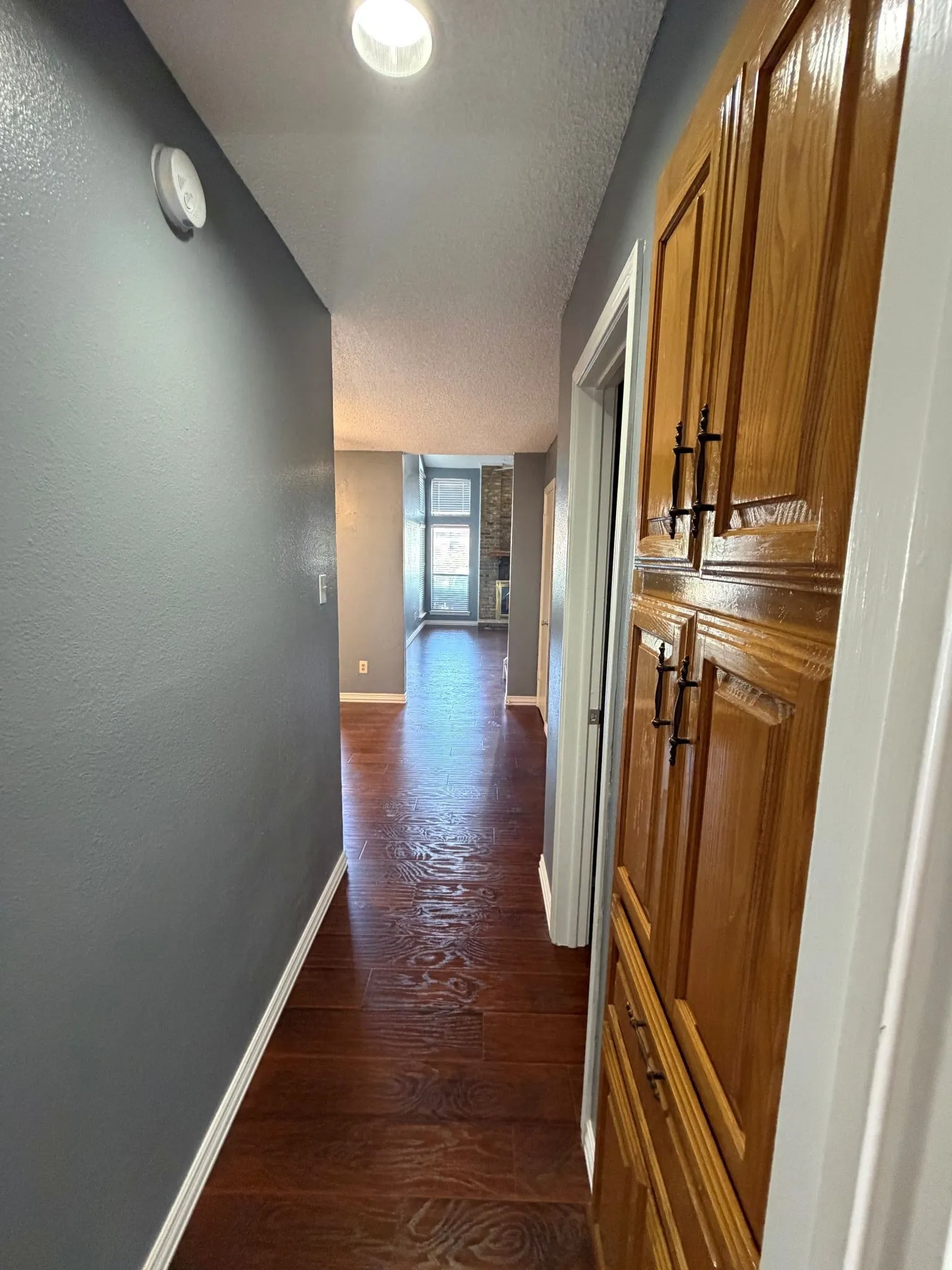 Hallway featuring wood-finish flooring, recessed ceiling lighting, and built-in wood cabinetry with dark hardware