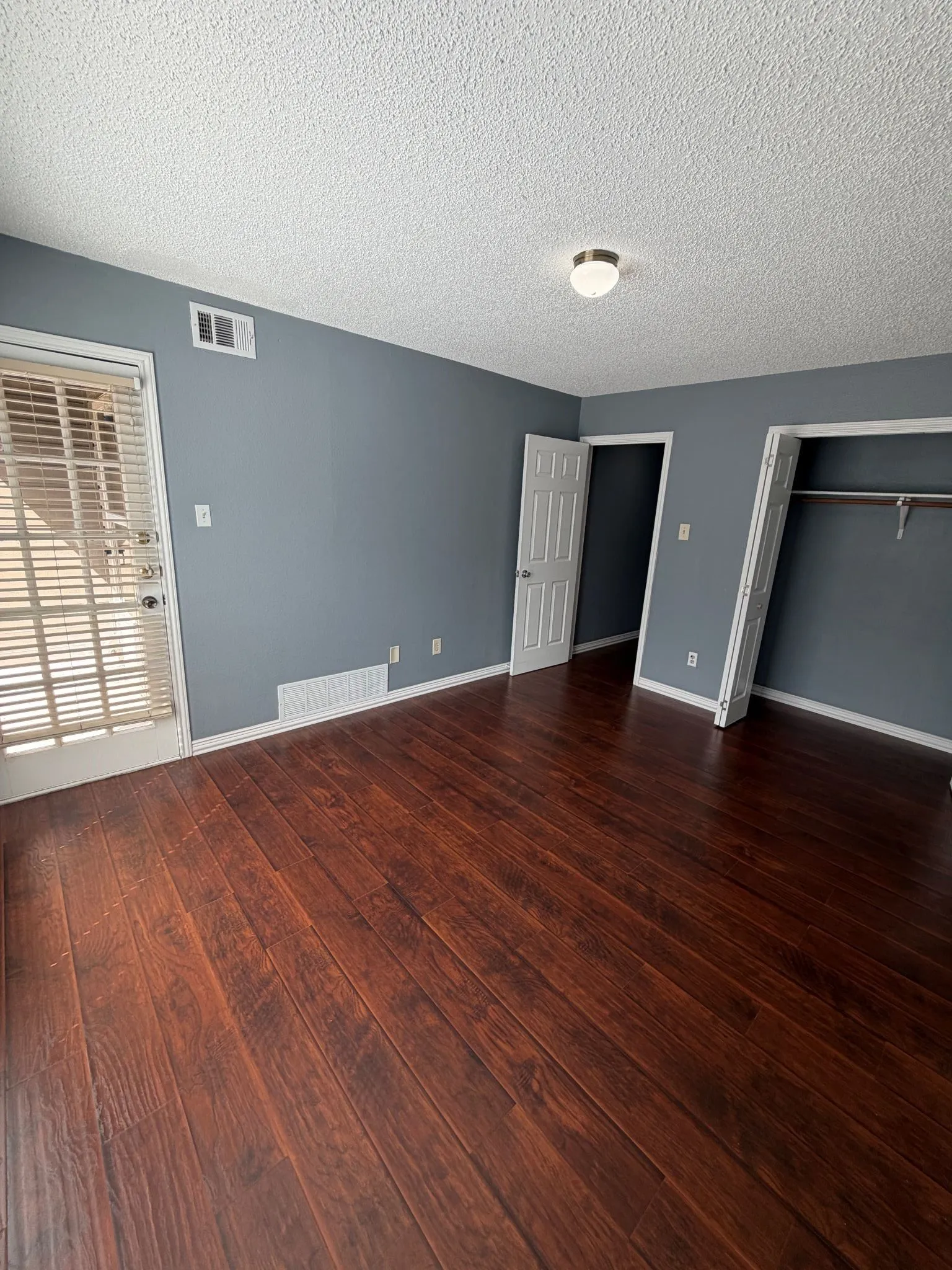 Interior space featuring dark-toned wood-finish flooring, neutral-hued walls, a multi-panel door, and a built-in closet with an integrated hanging rod