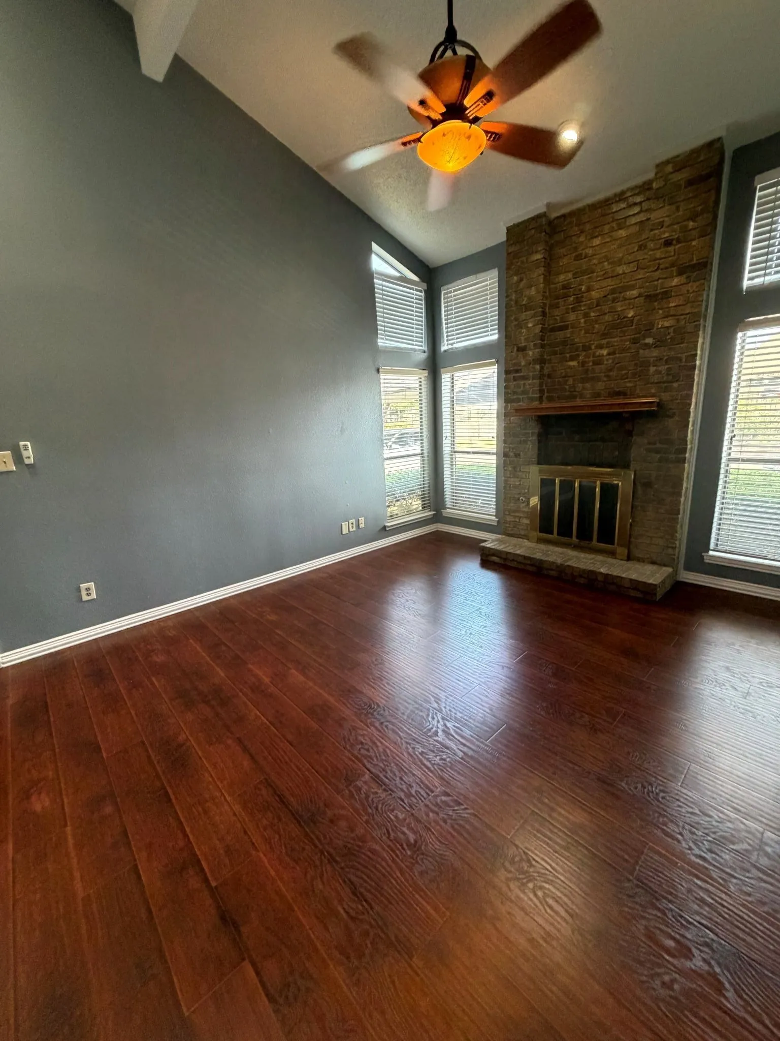 Vaulted ceiling featuring wood-finish flooring, floor-to-ceiling brick masonry fireplace, elevated mantel, and multi-pane windows