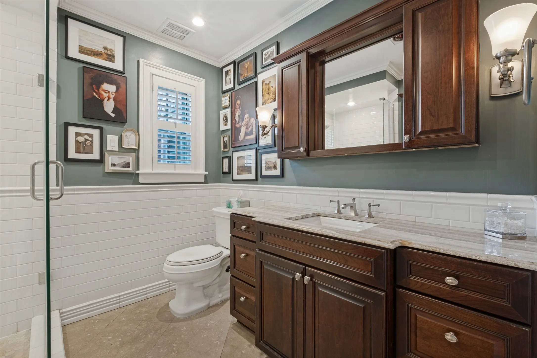 Custom dark wood vanity with stone countertop, integrated cabinetry, subway tile wall wainscoting, and glass-enclosed shower