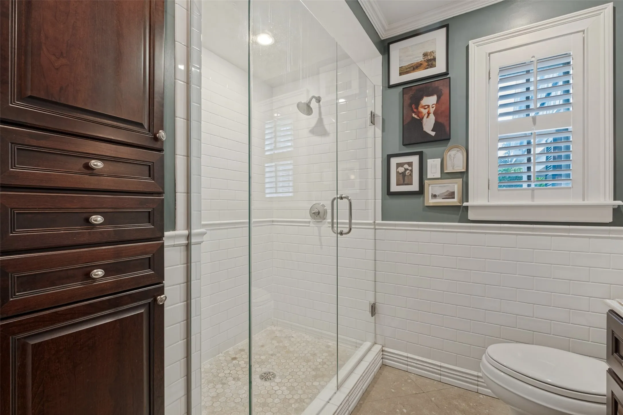 Walk-in shower featuring a glass enclosure, white subway tile surround, and stone pebble flooring, complemented by dark wood cabinetry and interior window shutters