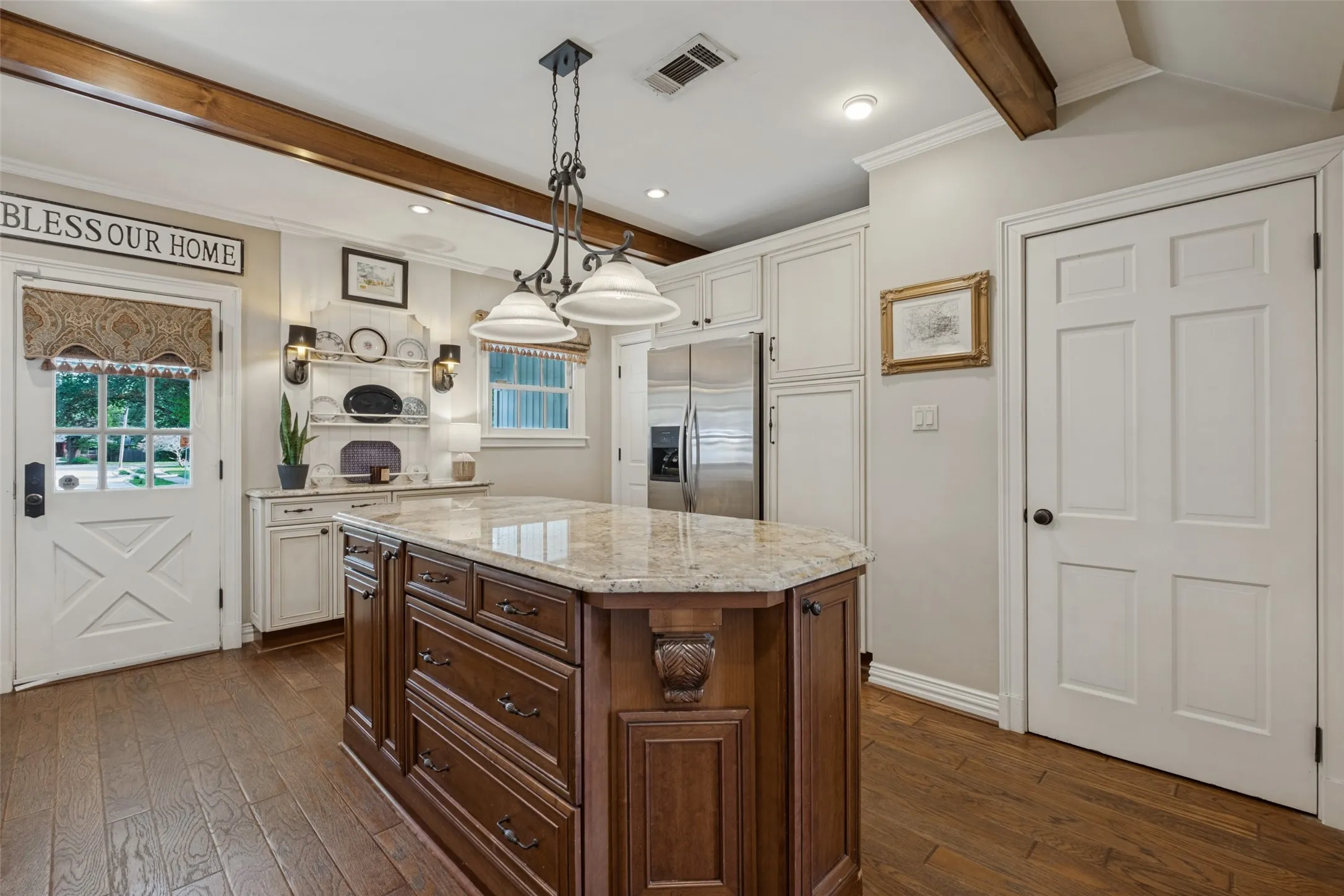 Kitchen featuring a center island with a natural stone countertop, wood-finish flooring, exposed stained wood ceiling beams, white shaker-style cabinetry, and a door with a decorative transom window