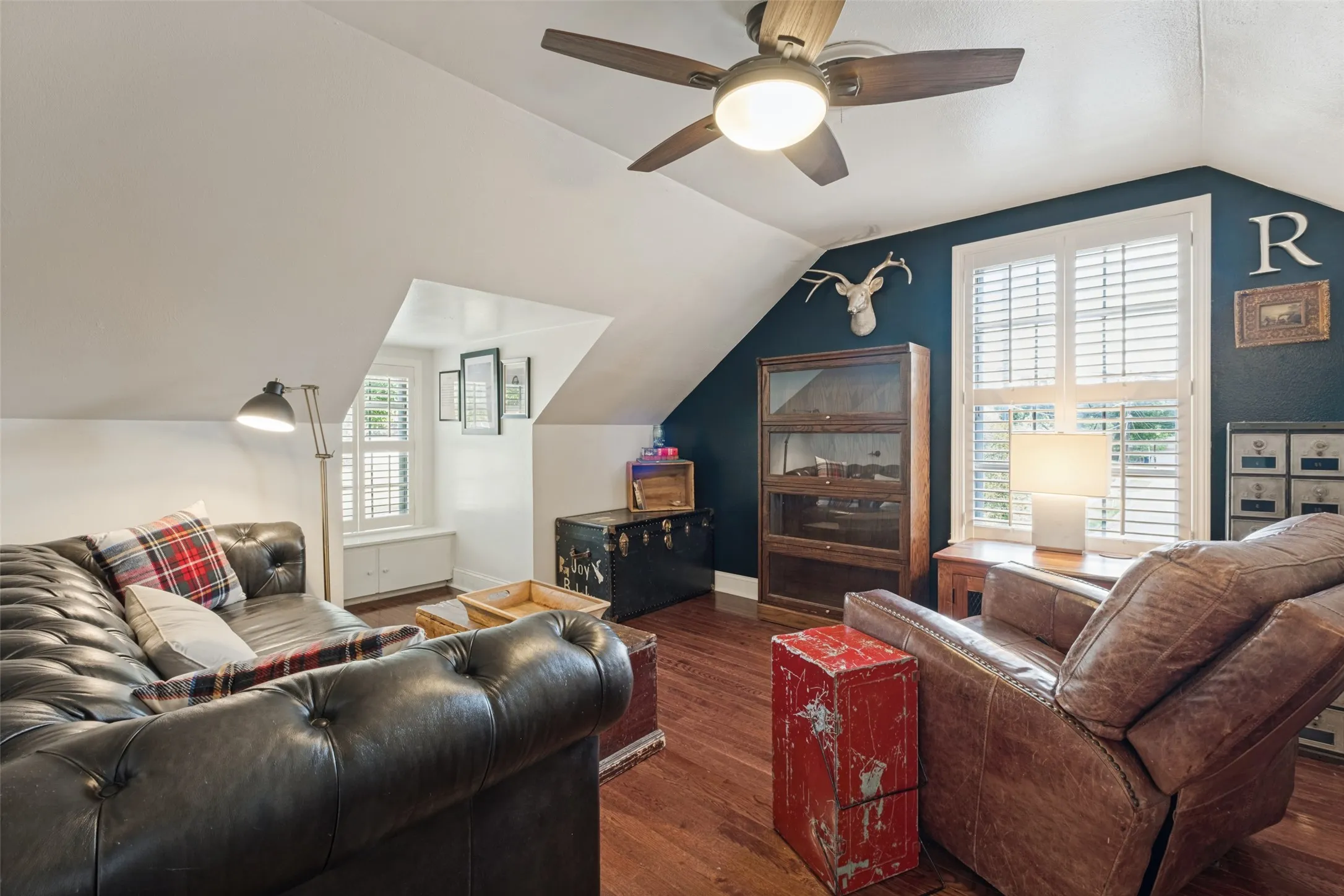 Vaulted ceilings featuring a central ceiling fan with integrated lighting, wood-finish flooring, and white plantation-style shutters