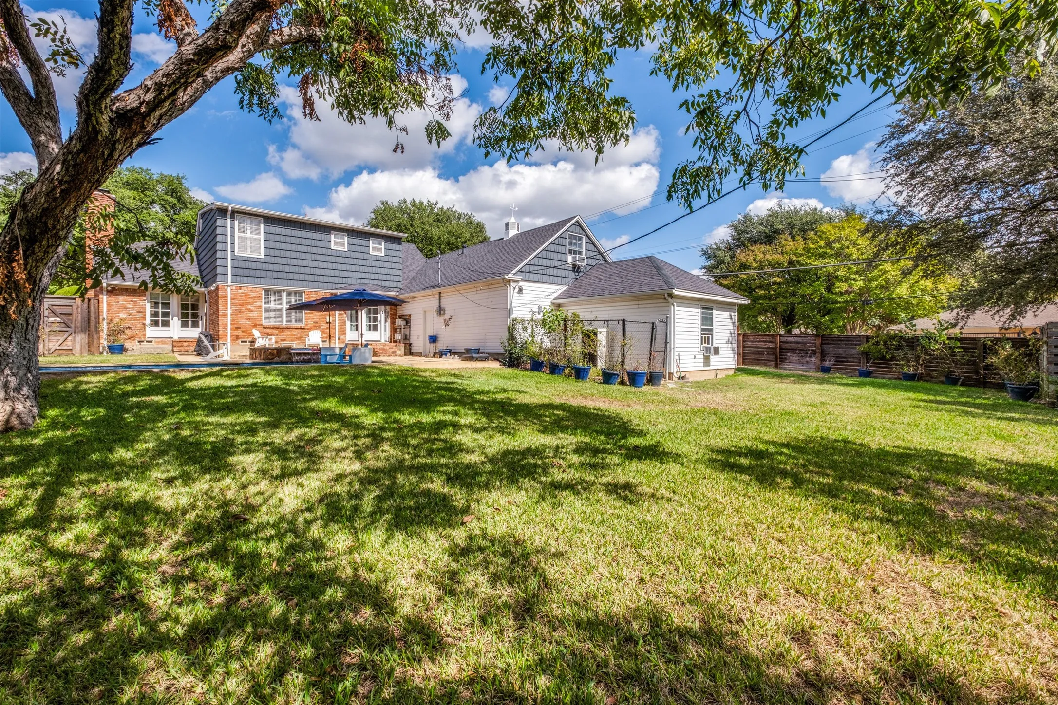 Expansive backyard featuring a large grass lawn, mature shade trees, and a wood privacy fence