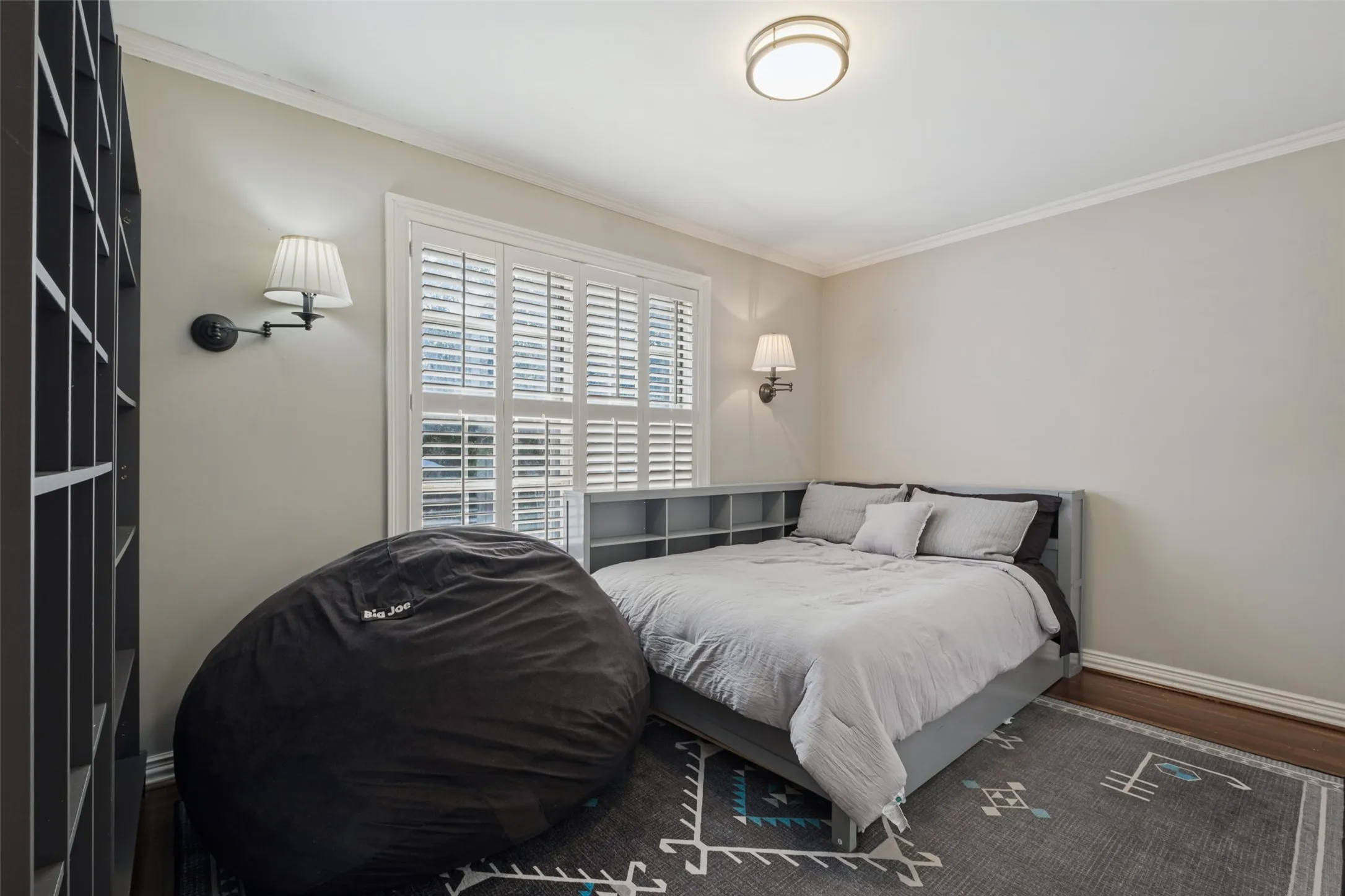 Room featuring wood-finish flooring, plantation shutters, dual wall-mounted sconces, and a ceiling-mounted light fixture