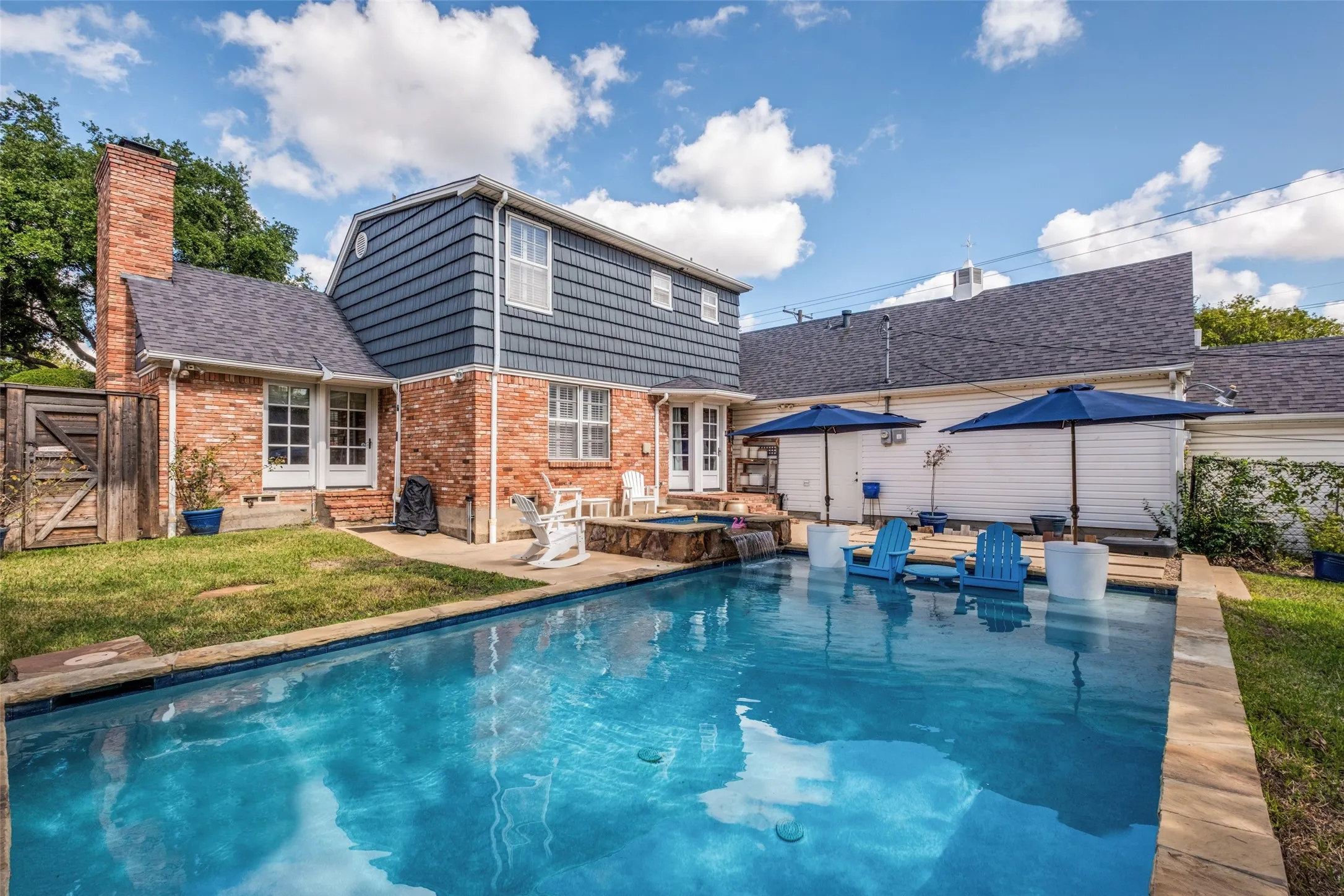Backyard featuring an in-ground pool with stone coping, raised spa, multi-textured exterior facade of brick and shingle siding, and a wood privacy fence