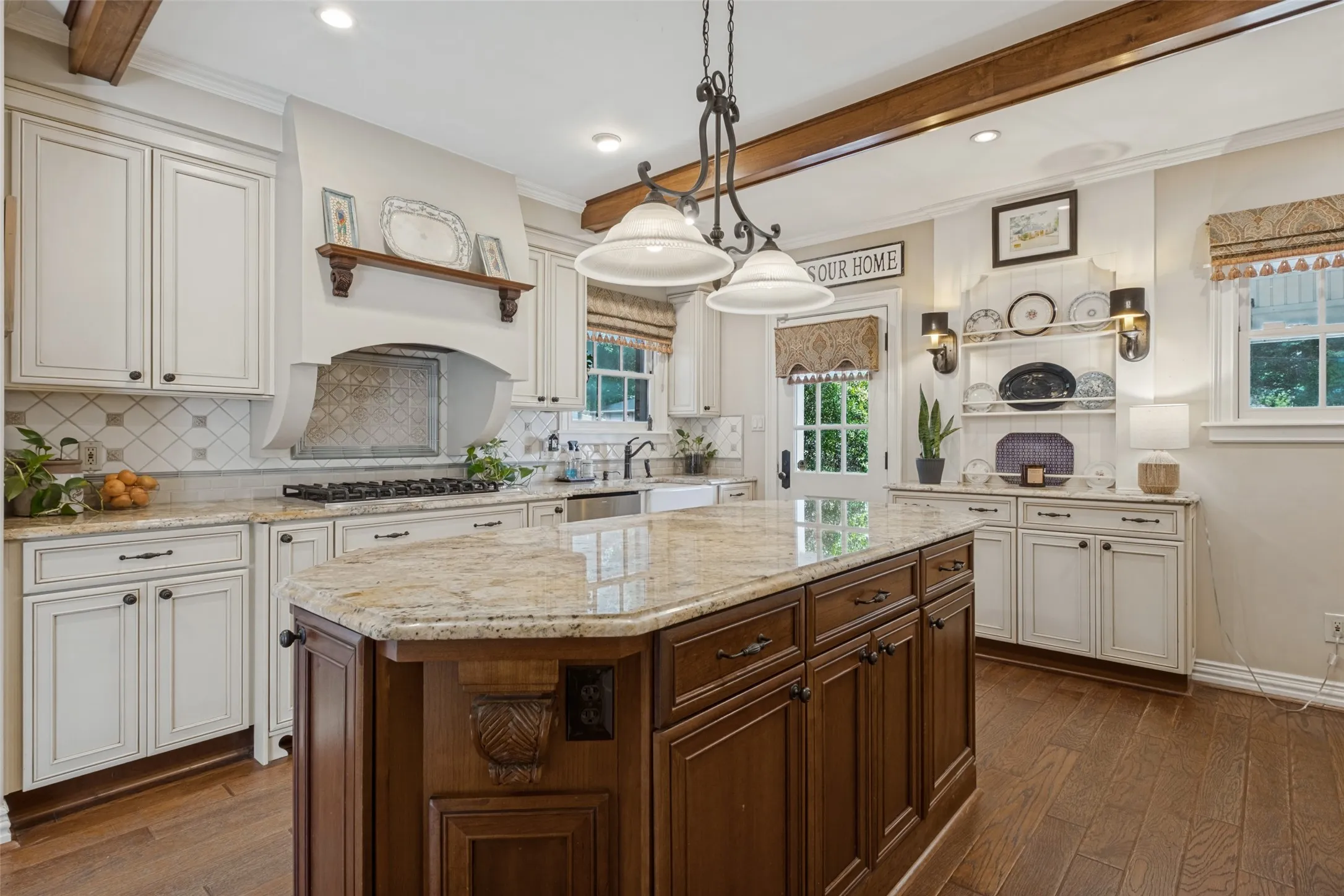 Kitchen featuring an expansive center island with stone countertops, wood-finish flooring, custom wood cabinetry, exposed decorative ceiling beams, and a farmhouse-style sink