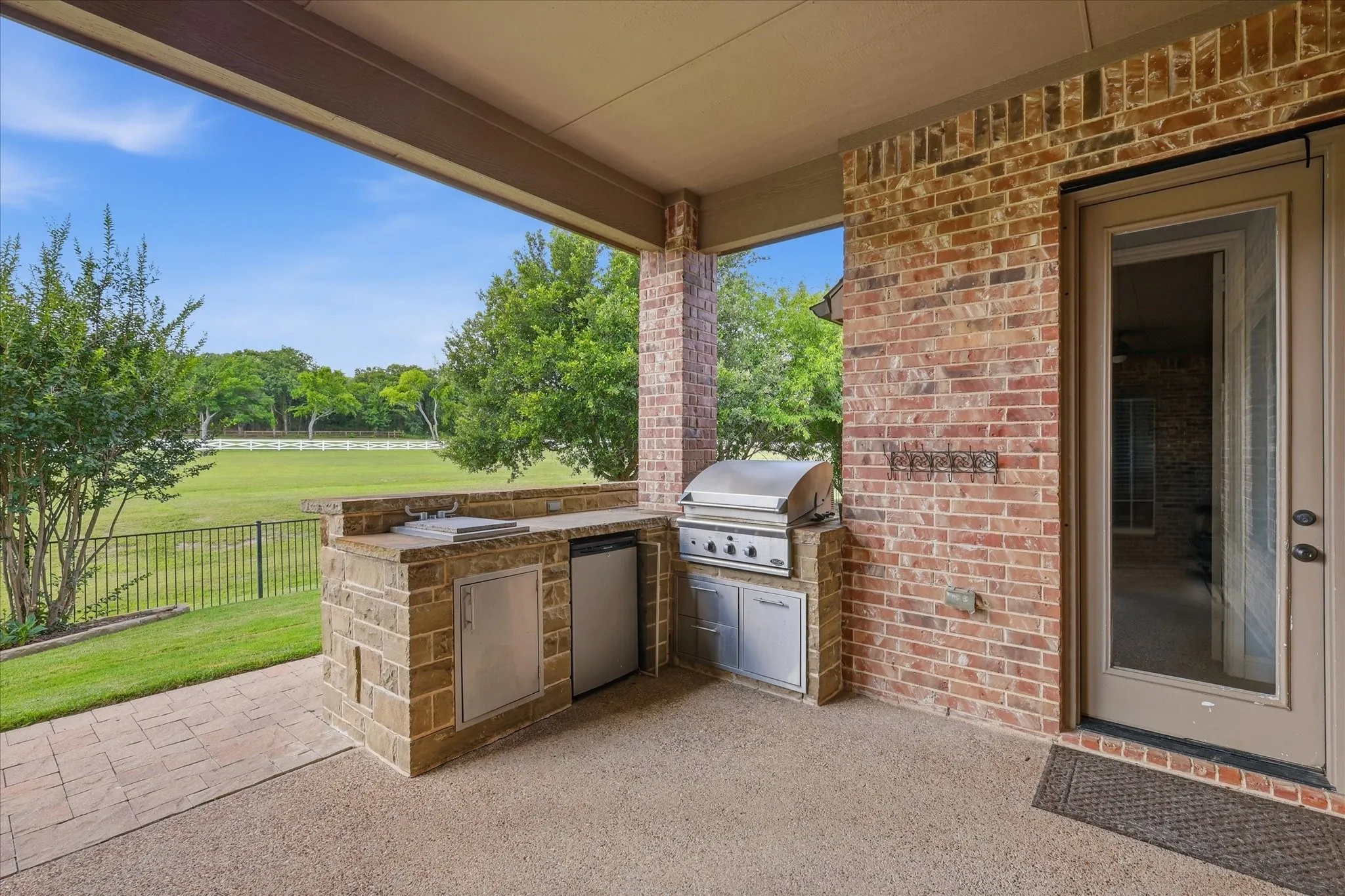 Covered patio featuring an outdoor kitchen with stone masonry, a stainless steel built-in grill, a compact refrigerator, and a stone countertop