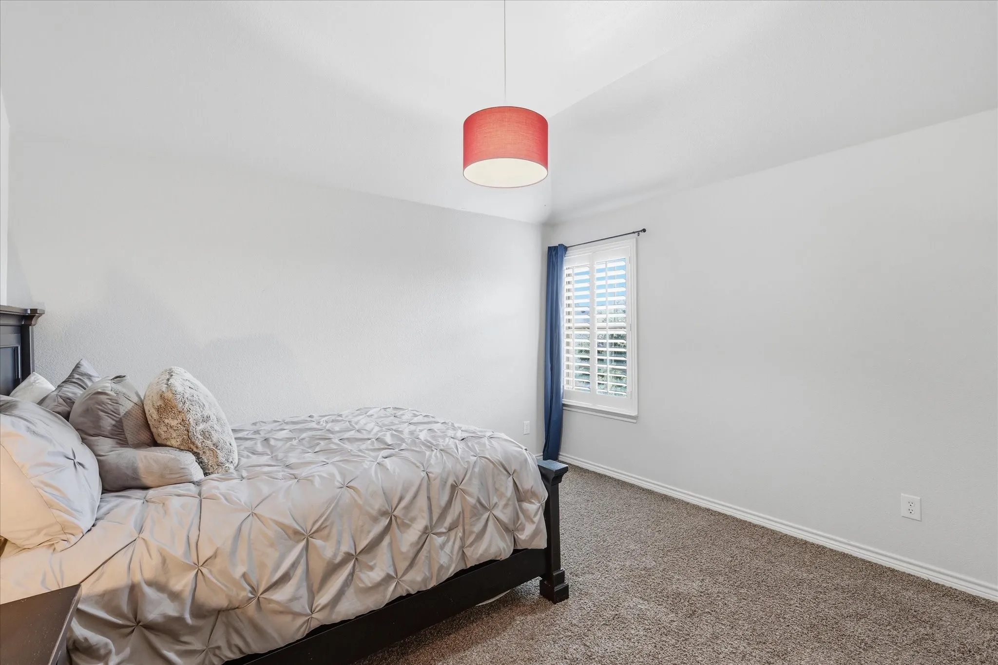 Neutral-toned wall-to-wall carpeting, vaulted ceiling, and window featuring white plantation shutters