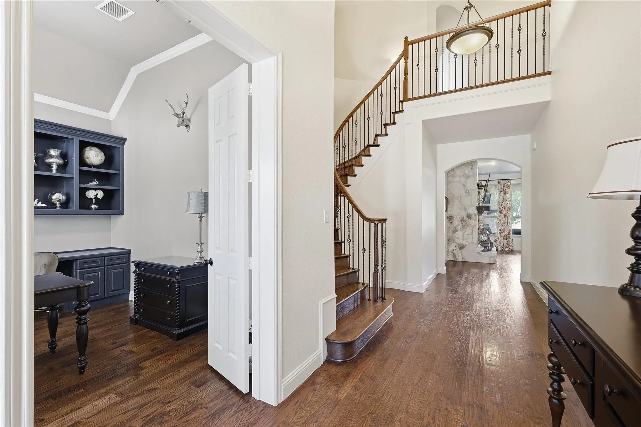 Foyer featuring wood-finish flooring, a curved staircase with wrought iron balusters, built-in cabinetry, and a vaulted ceiling