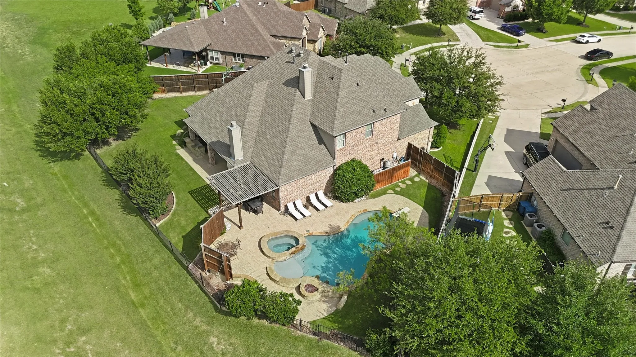 Brick exterior residence featuring an in-ground pool with an integrated spa, stone-paved patio, covered pergola, and a fenced yard