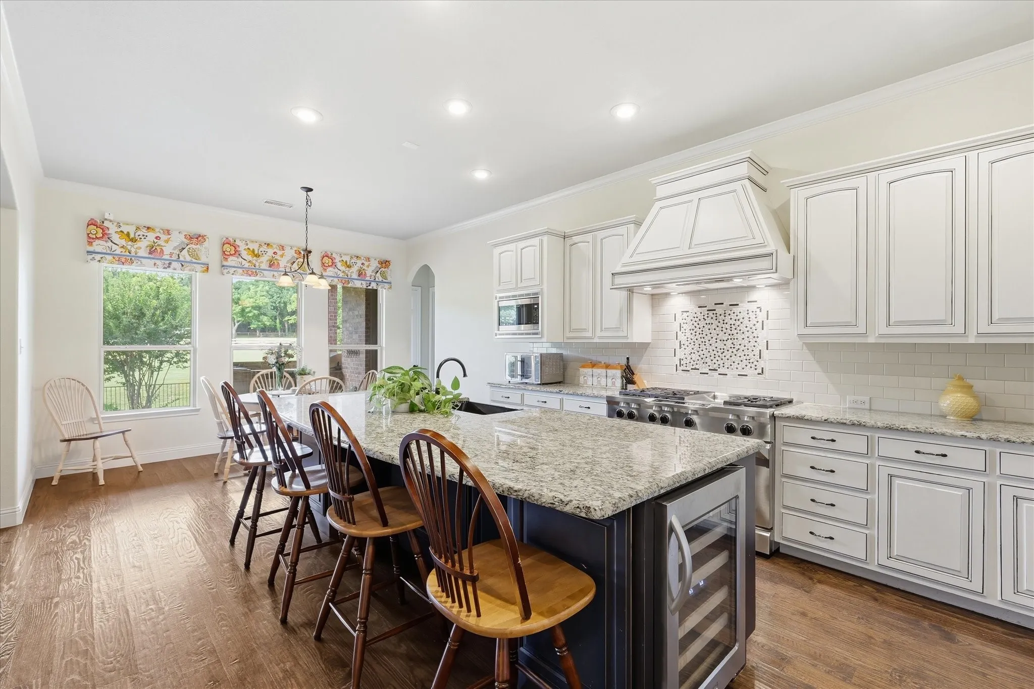 Kitchen featuring a central island with stone countertop, custom cabinetry, professional-grade range with decorative hood, stone-style tile backsplash, and wood-finish flooring