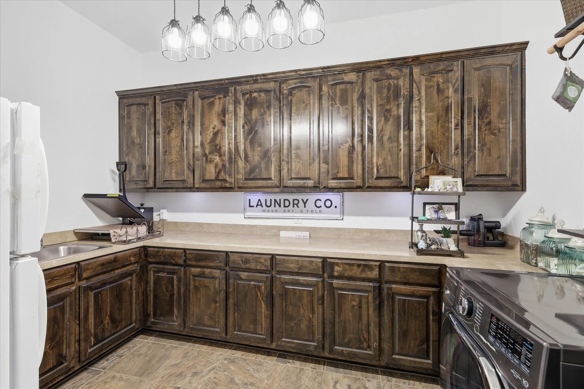 Custom stained-wood cabinetry, extended solid-surface countertop, integrated stainless steel sink, multi-pendant glass lighting, and ceramic tile flooring