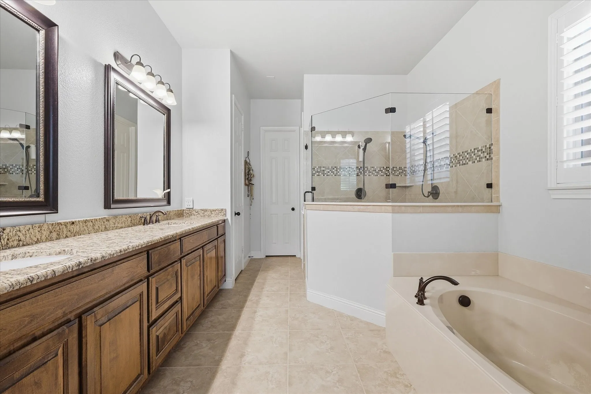 Bathroom featuring a dual-sink vanity with stone countertop, wood cabinetry, built-in soaking tub with deck-mounted faucet, and a tiled shower enclosure with glass surround