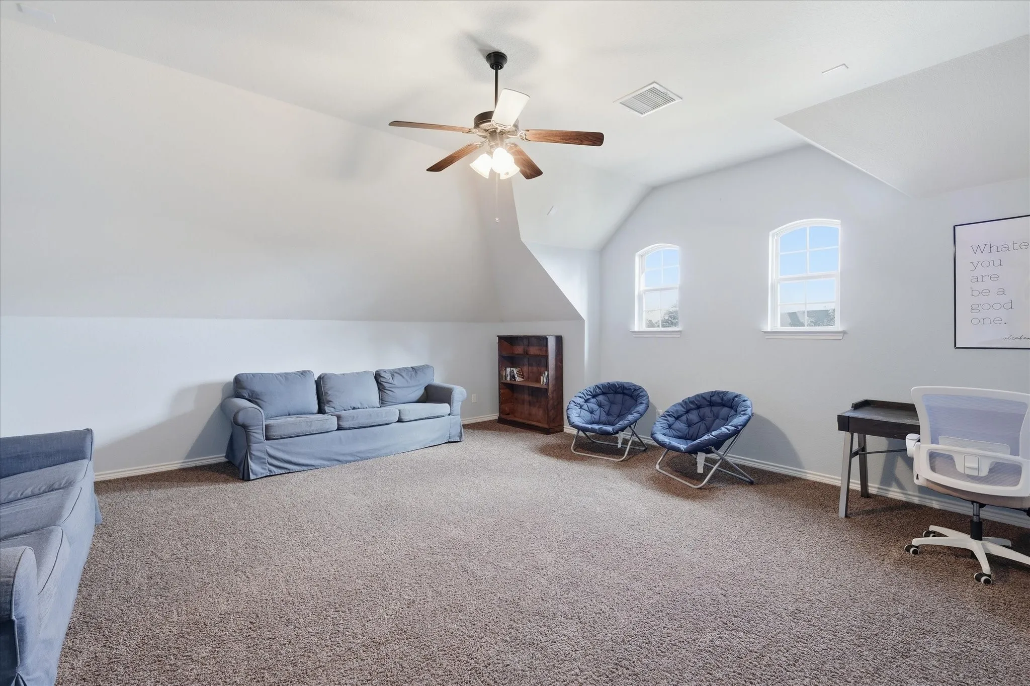 Spacious room featuring vaulted ceilings, neutral wall tones, arched windows, and a ceiling fan with integrated lighting