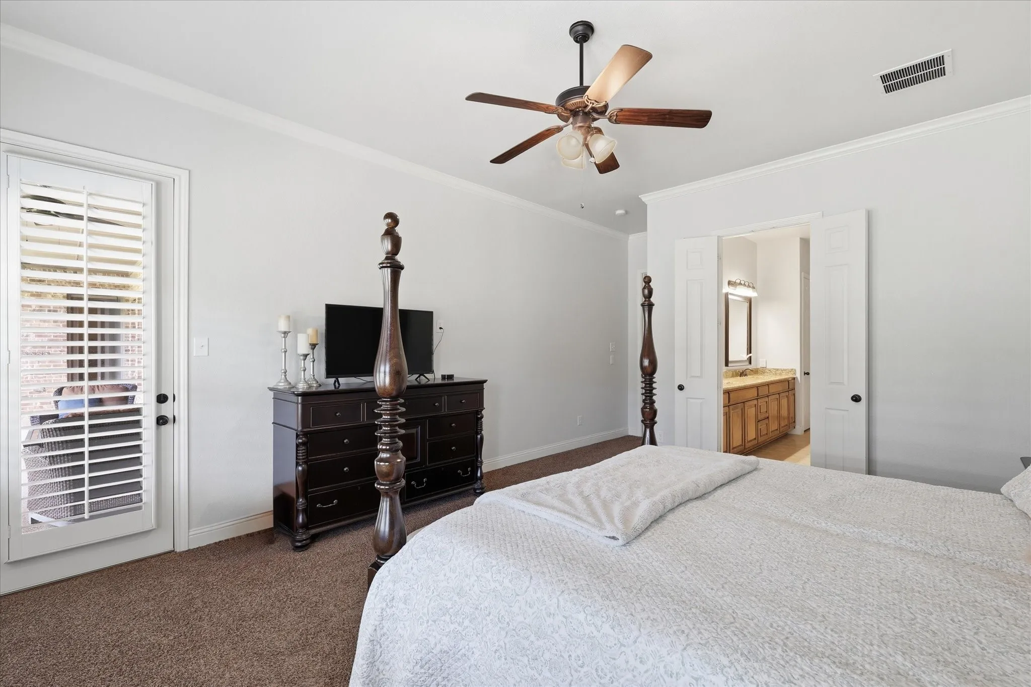 Primary bedroom featuring carpeted flooring, a ceiling fan with integrated lighting, and a glass-paneled door with plantation shutters