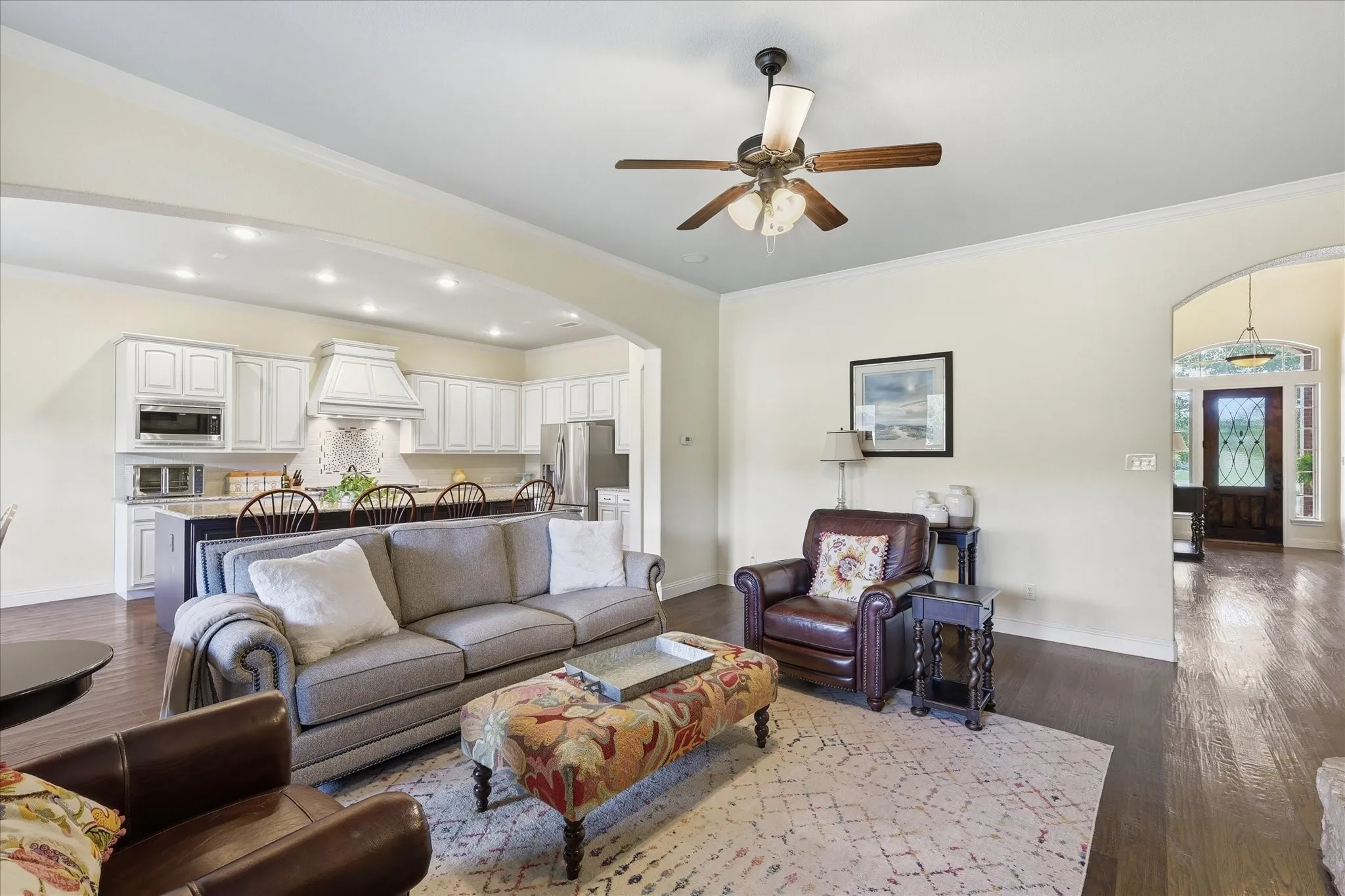 Open-concept space featuring dark wood-finish flooring, an arched entryway, recessed lighting, and a ceiling fan with integrated lighting, extending to a kitchen area with white cabinetry and a center island