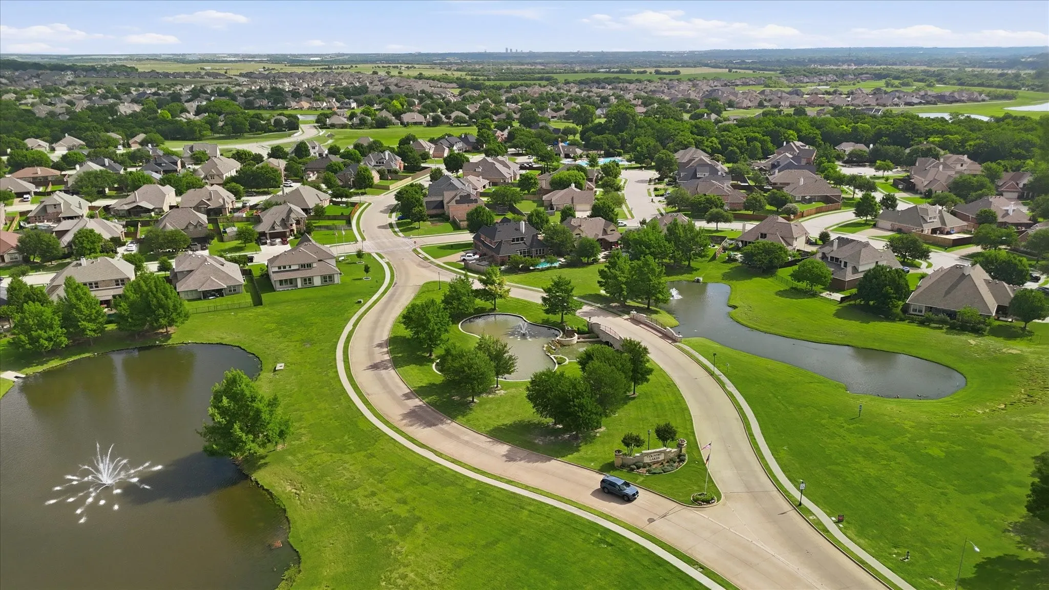 Aerial perspective of the neighborhood featuring sprawling green spaces, multiple ponds, decorative water fountains, and mature trees