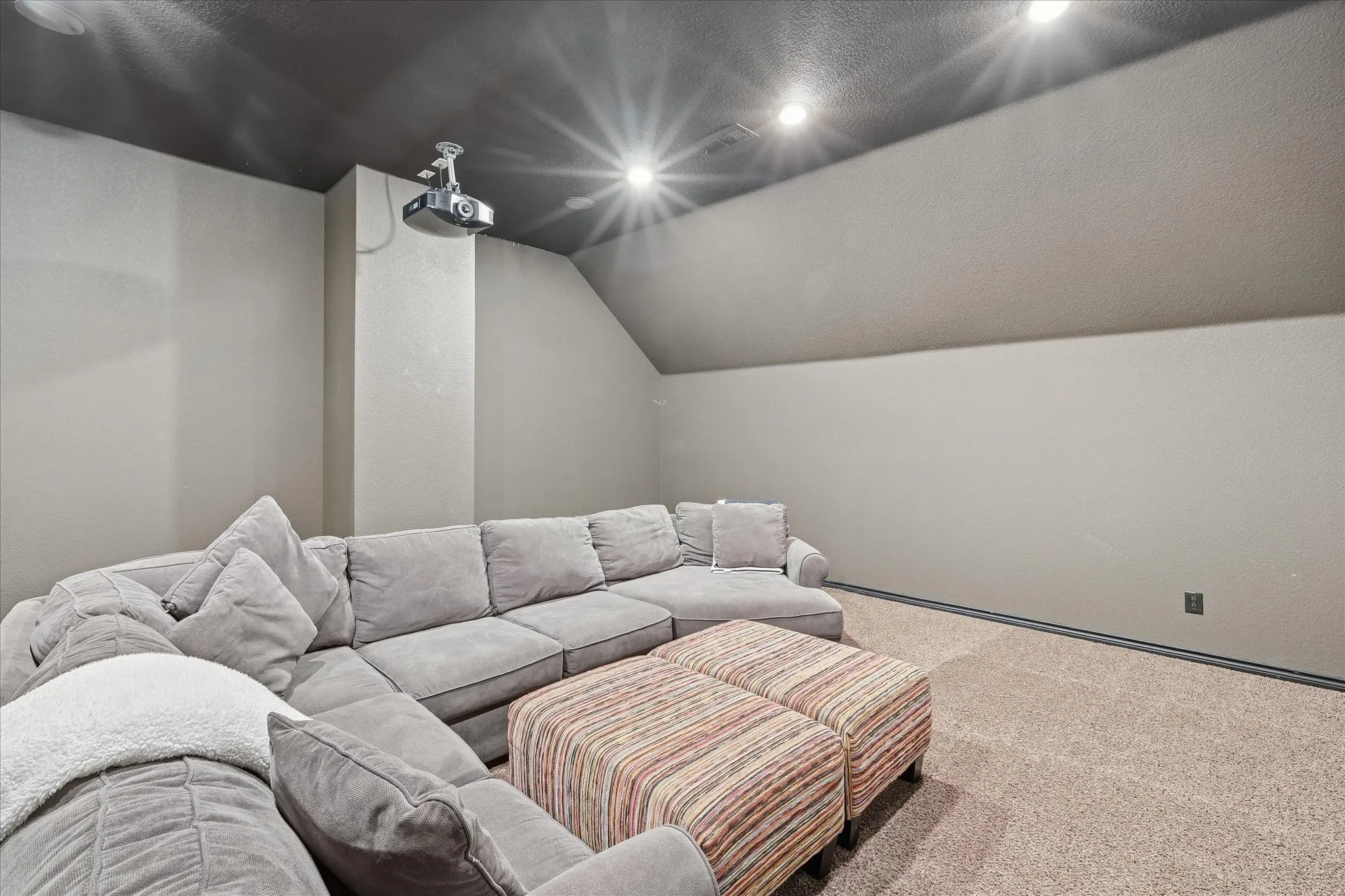 Dedicated room featuring a dark-toned ceiling, neutral wall finishes, recessed lighting, and a ceiling-mounted projector