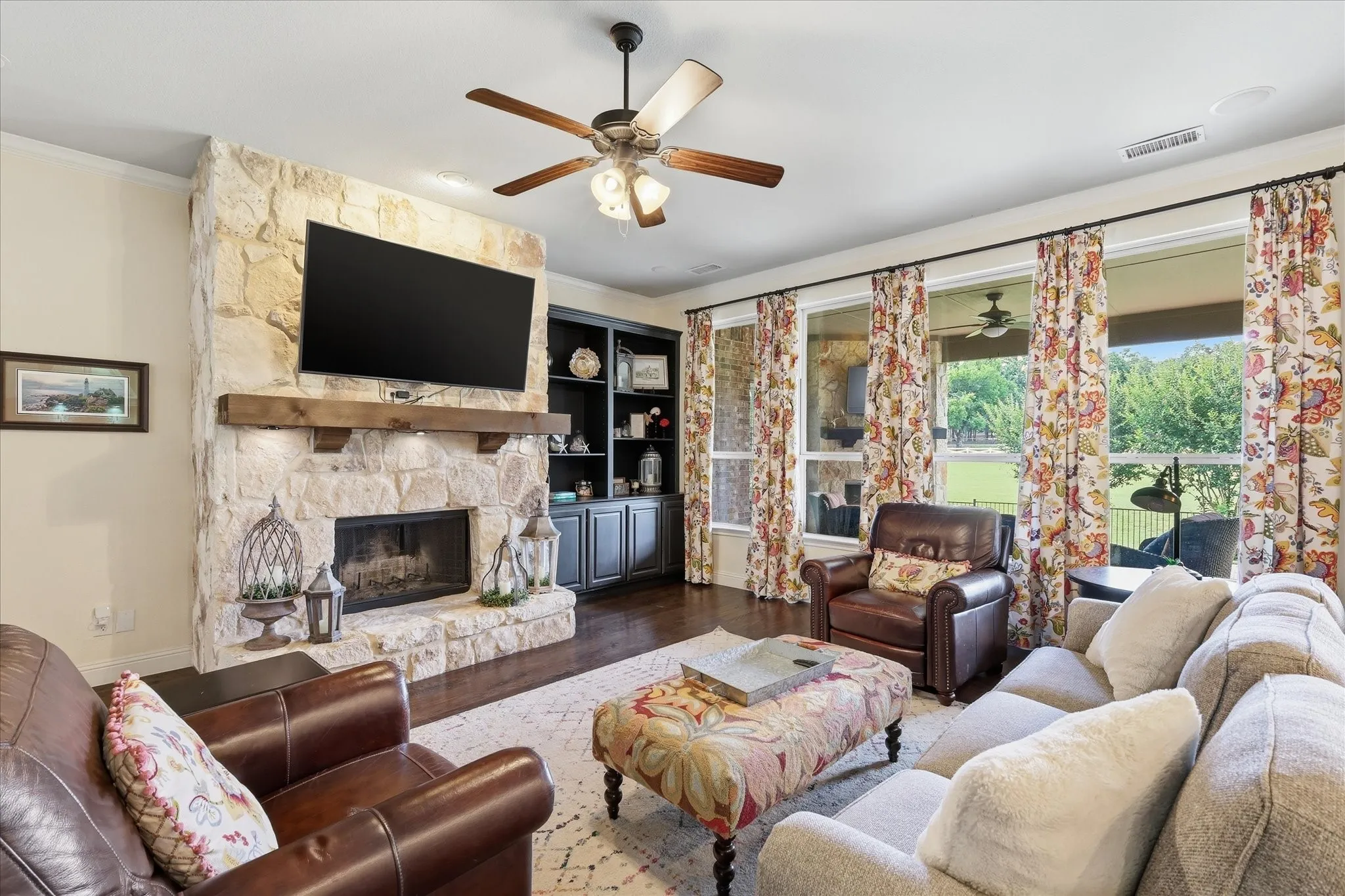 Full-height natural stone fireplace with a thick timber mantel, built-in dark wood shelving, wood-finish flooring, and large windows