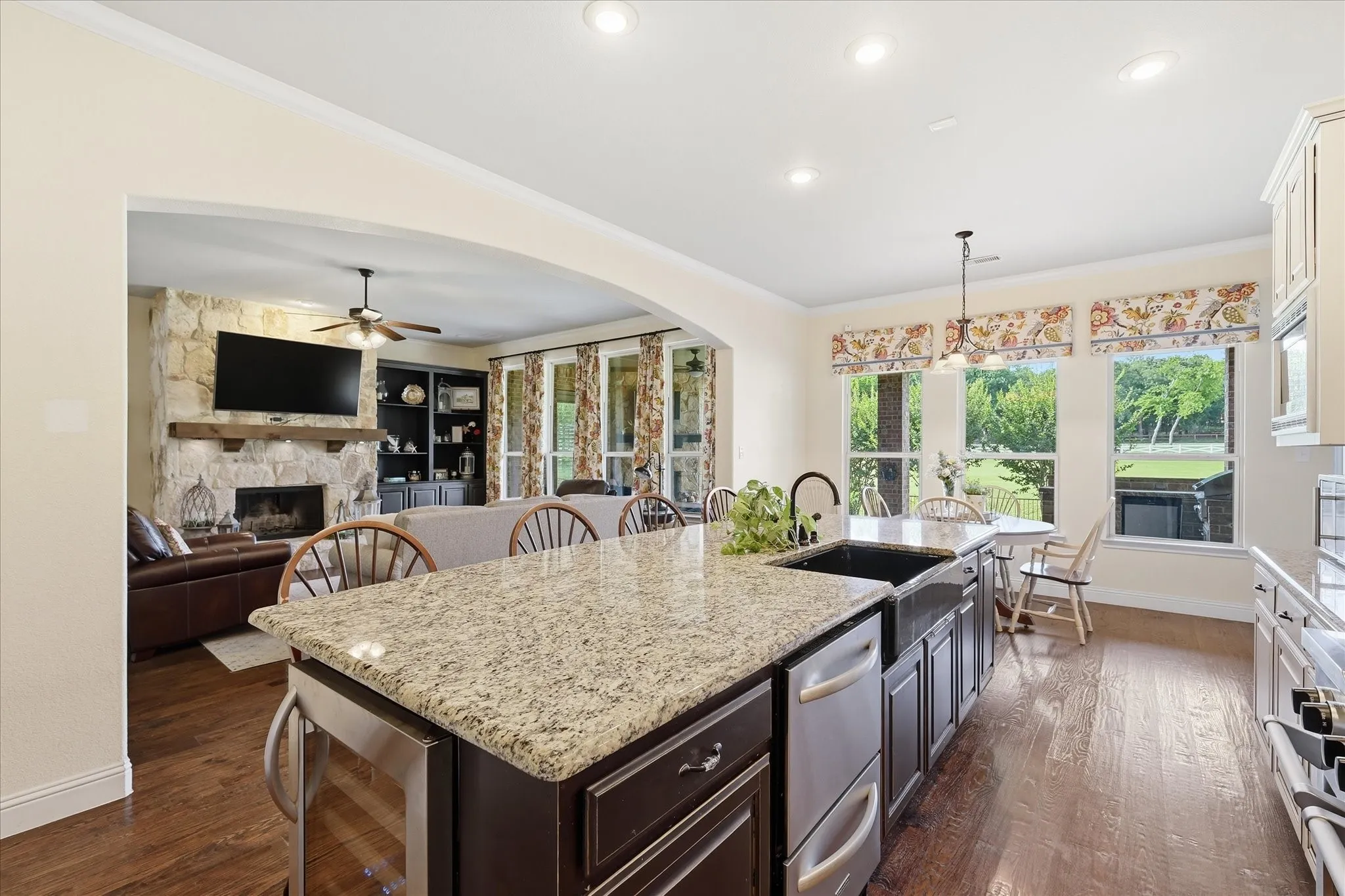 Kitchen featuring a stone-topped island with an integrated farmhouse sink, dark wood cabinetry, recessed lighting, and wood-finish flooring, complemented by a floor-to-ceiling stone fireplace