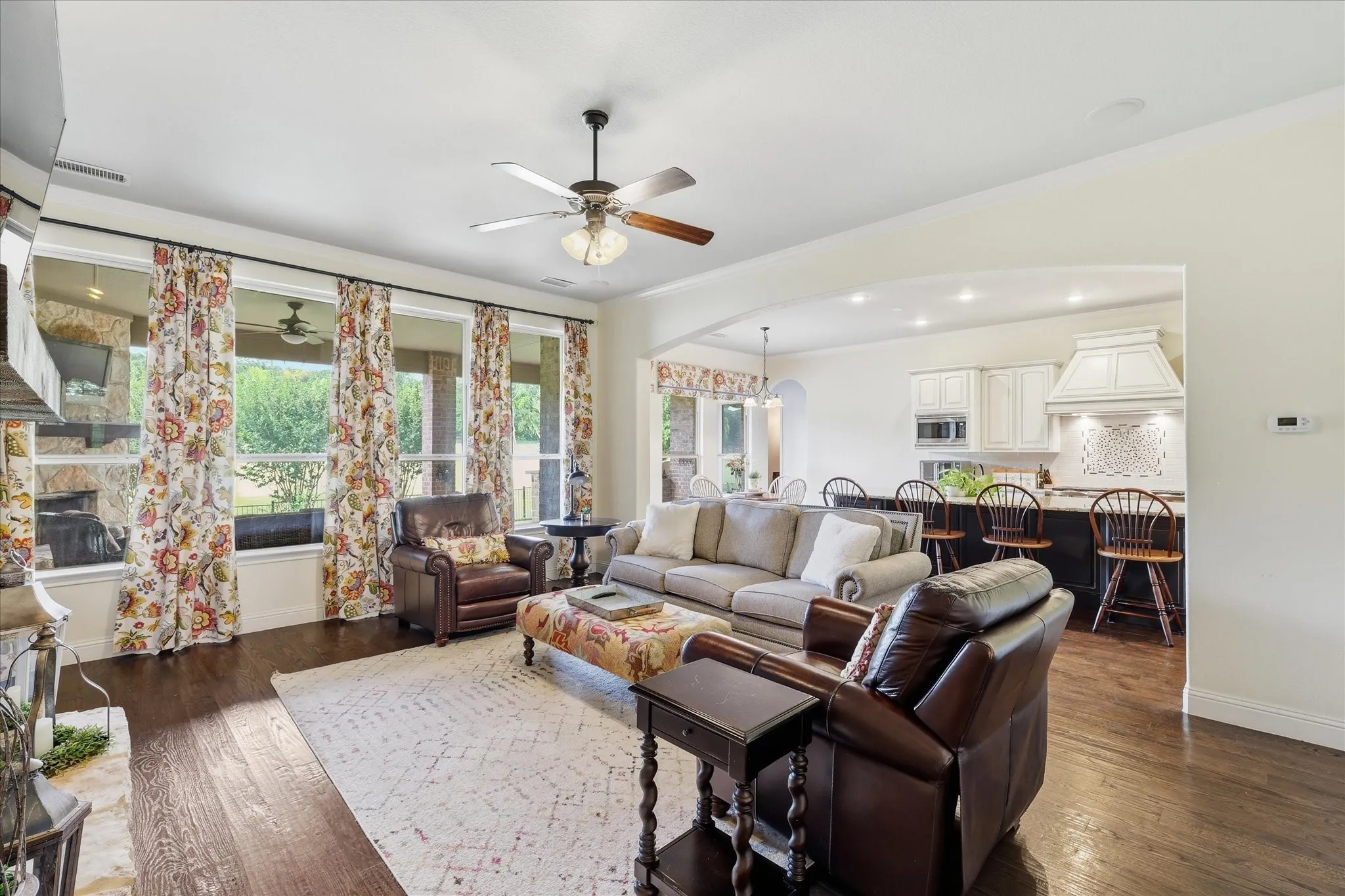 Open-concept living space featuring wood-finish flooring, a stone-surround fireplace, a ceiling fan, and oversized windows