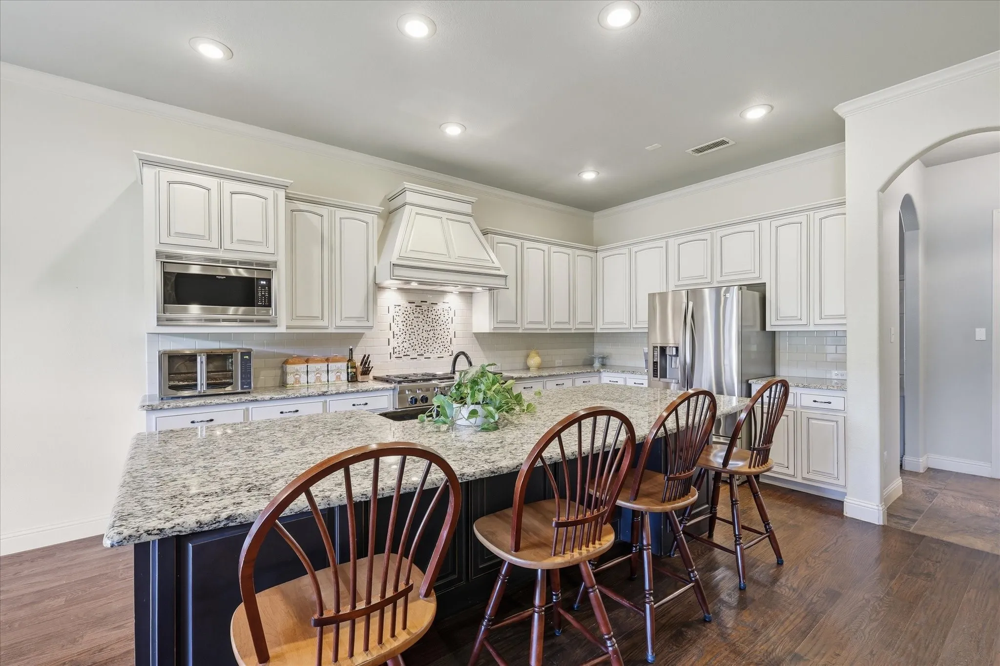 Kitchen featuring a central island with stone countertop, white cabinetry with crown molding, stainless steel appliances, decorative tile backsplash, and wood-finish flooring