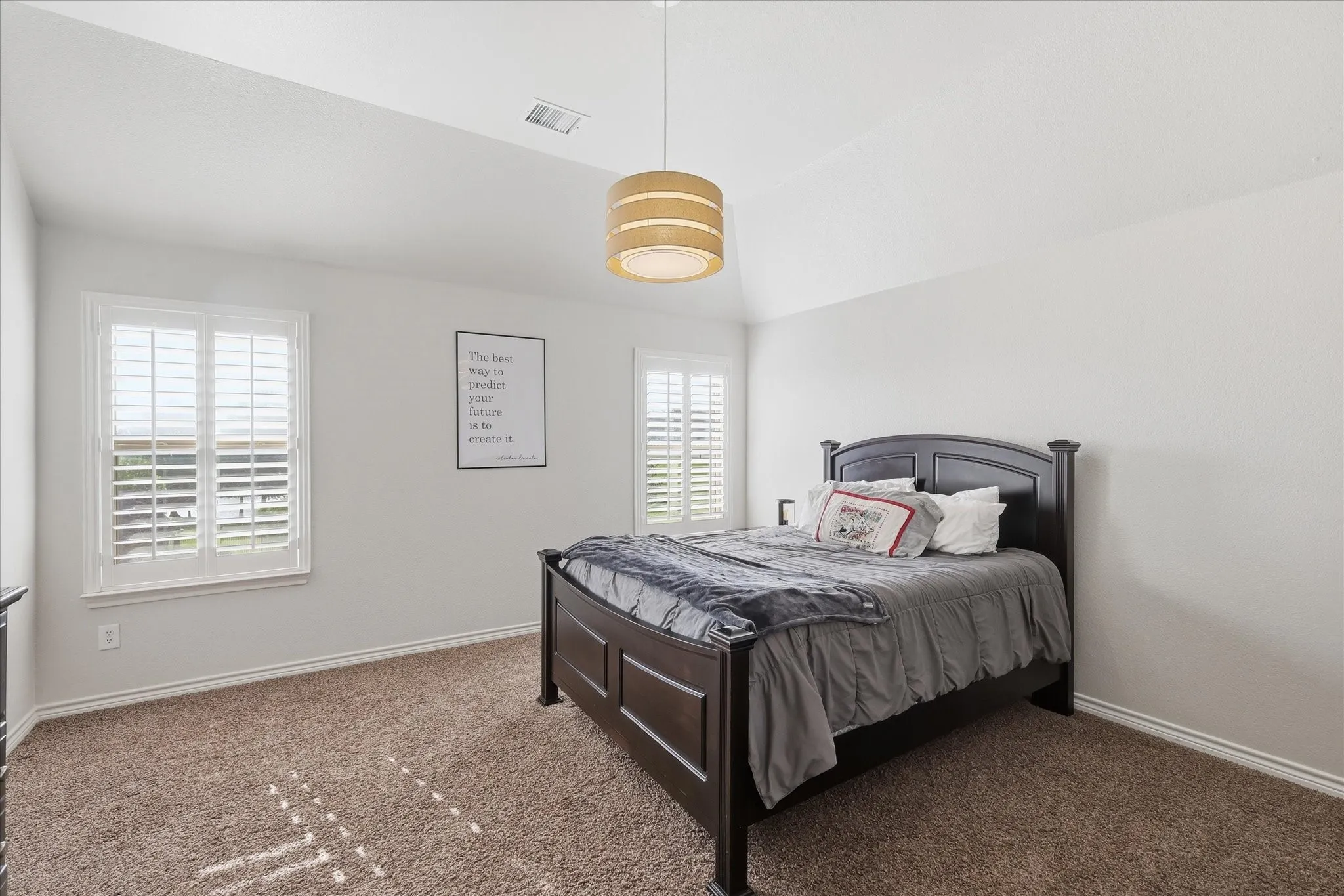 Vaulted ceiling featuring a cylindrical tiered pendant light fixture, dual windows with plantation shutters, and wall-to-wall carpeting