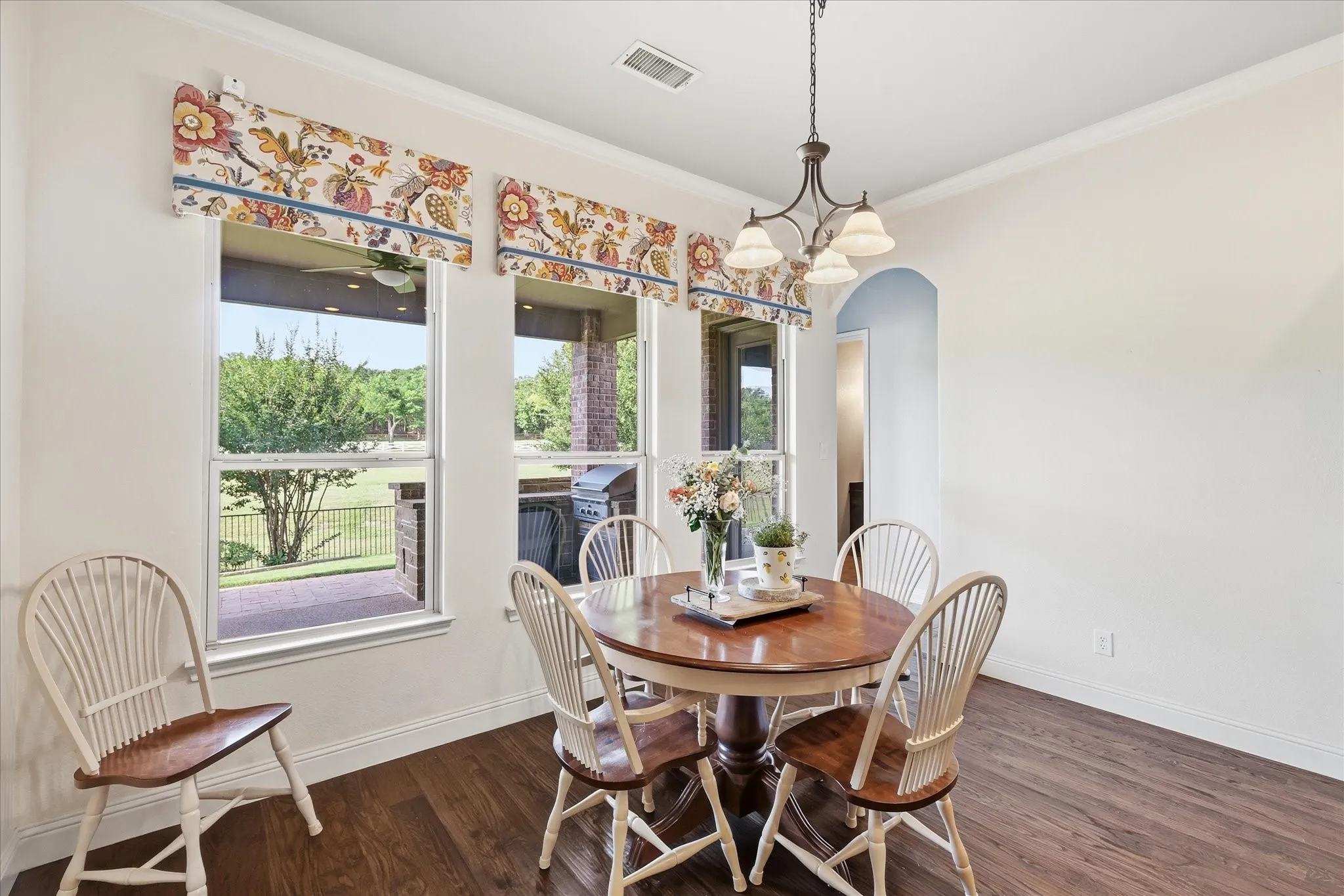 Dining area featuring wood-finish flooring, crown molding, a multi-arm chandelier, and three large windows with arched entryway detail