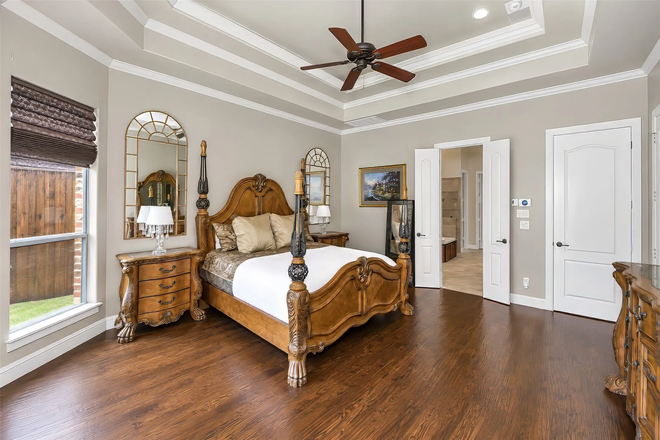 The primary bedroom features a tiered ceiling detail and wood flooring.