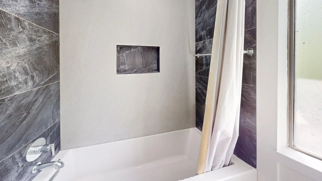 Bathtub with polished chrome fixtures, integrated wall niche, and contrasting large-format dark stone-finish and neutral-tone tile surrounds
