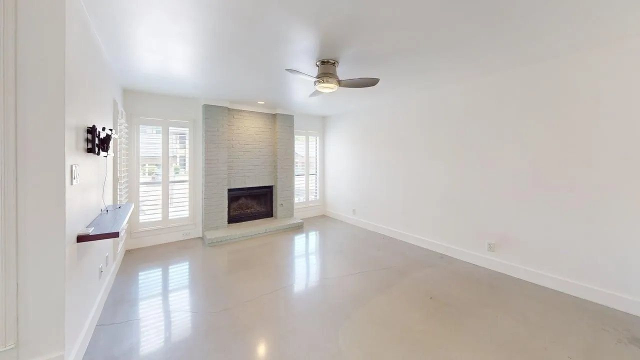 Living area featuring polished concrete flooring, a floor-to-ceiling painted brick fireplace, a built-in wall-mounted shelf, plantation shutters, and a central ceiling fan