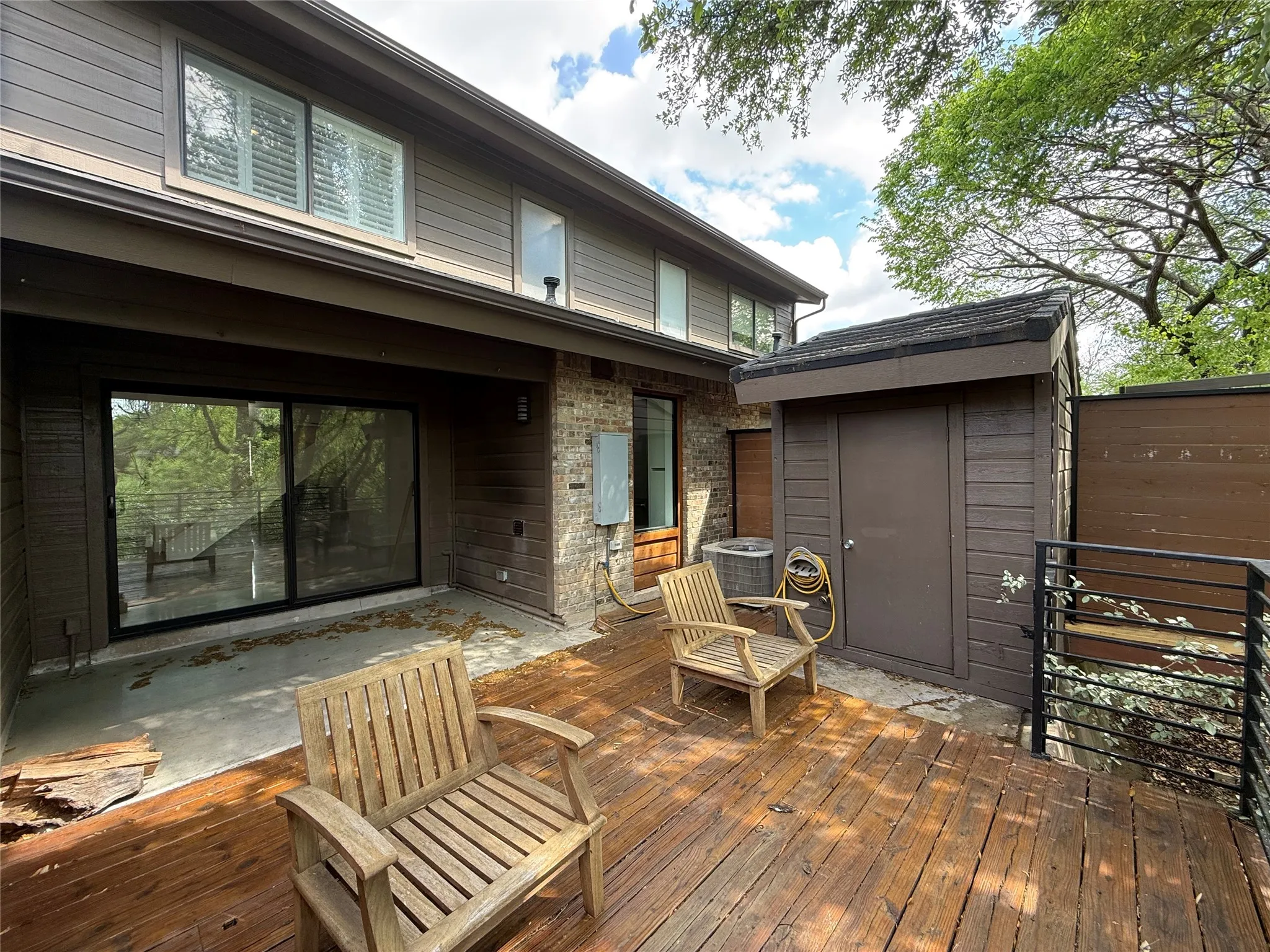 Multi-level wood deck with horizontal railing, brick exterior cladding, sliding glass doors, and attached exterior storage structure