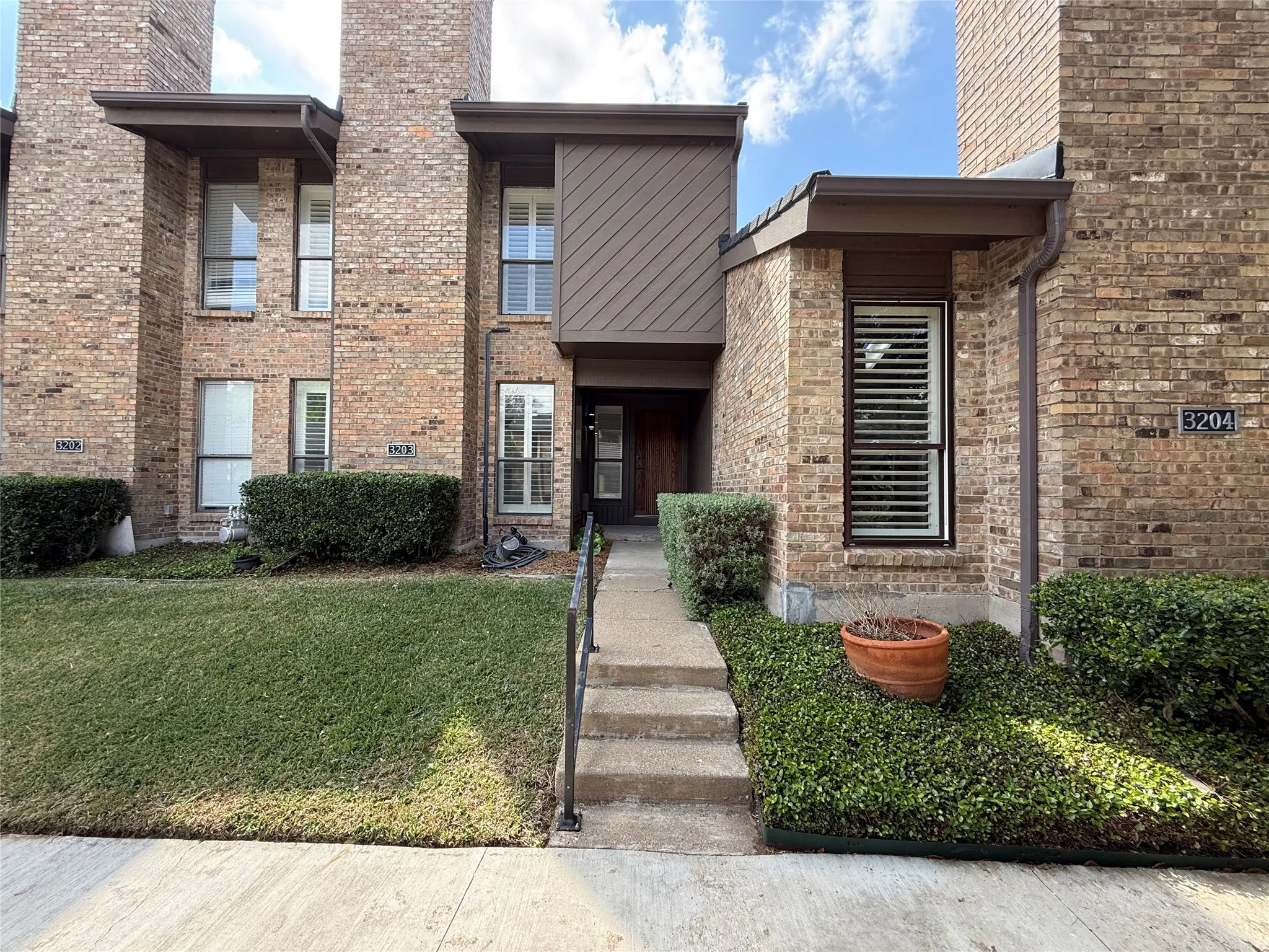 Multi-level brick exterior featuring vertical wood siding, tall chimneys, and metal-framed windows with plantation-style shutters