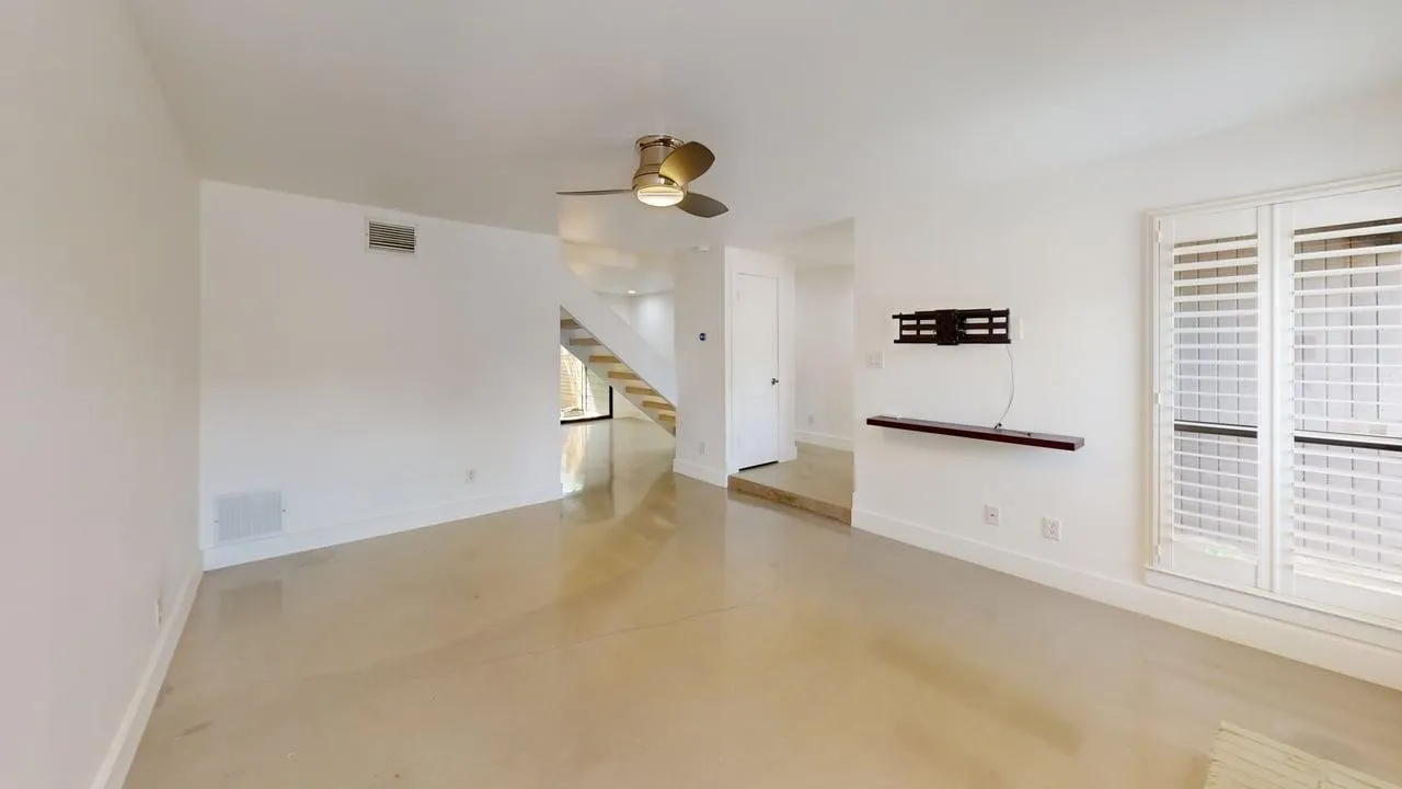 Polished concrete flooring, ceiling fan with integrated lighting, wall-mounted floating shelf, and plantation shutters