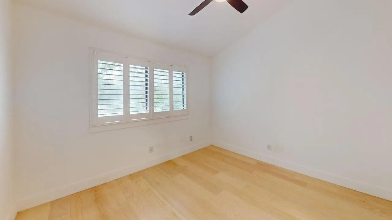 Room featuring vaulted ceilings, wood-finish flooring, and white plantation shutters, complemented by a ceiling fan