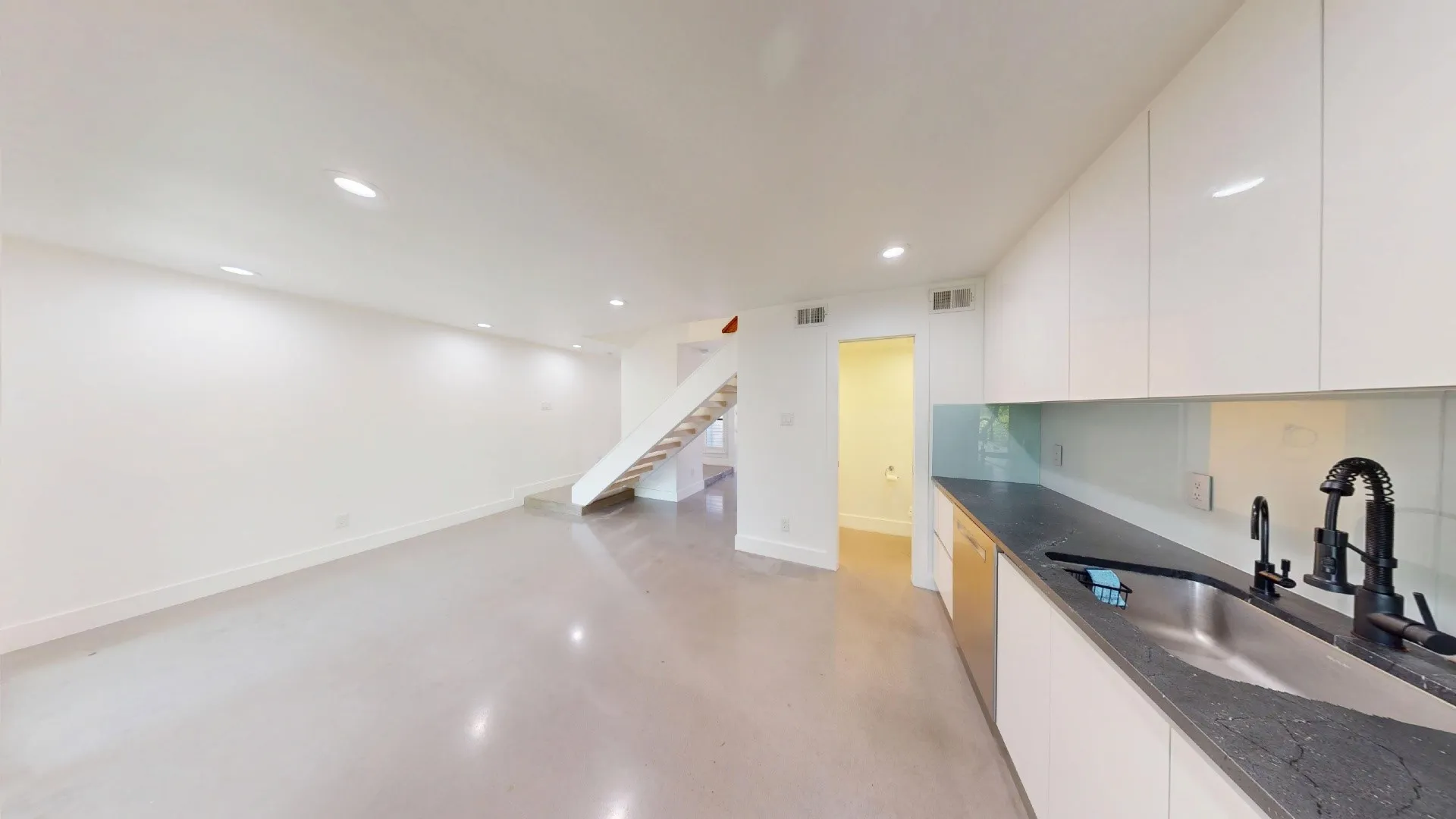 Kitchen featuring high-gloss cabinetry, dark stone countertops, a glass backsplash, and an undermount stainless steel sink with a matte black faucet
