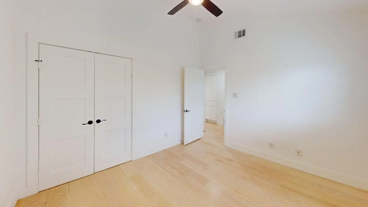 Interior space featuring wood-finish flooring, vaulted ceilings, double-panel closet doors with matte black hardware, and an integrated ceiling fan