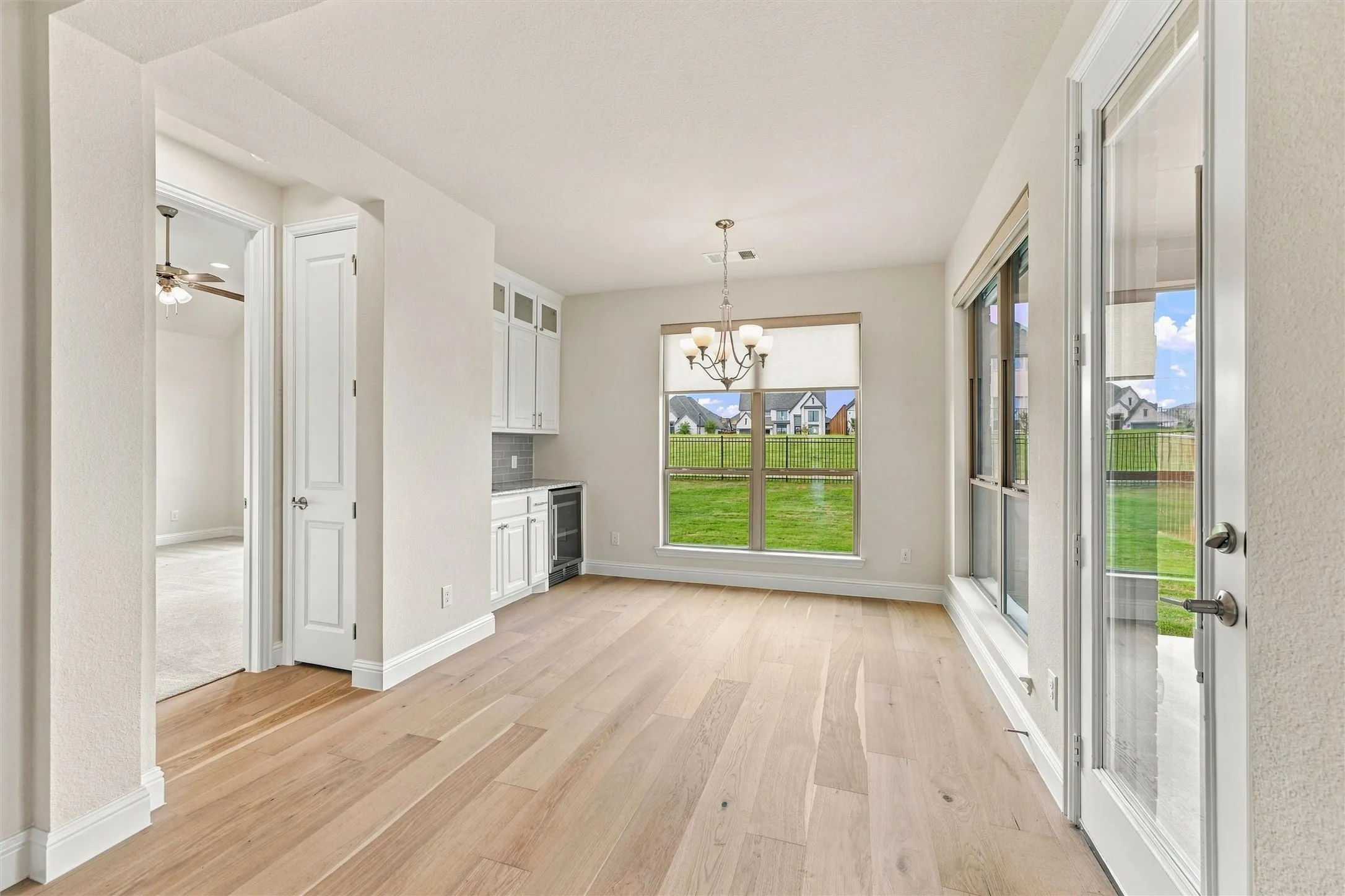 Light-filled space featuring wood-finish flooring, a built-in cabinetry unit with an integrated beverage cooler, a multi-arm chandelier, and a glass-paned exterior door