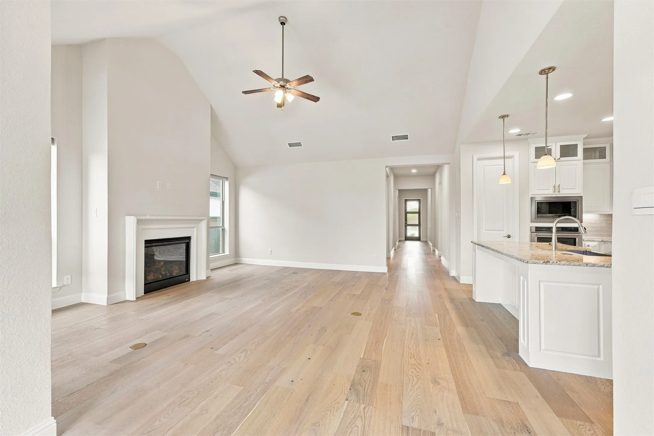 Vaulted ceilings, wood-finish flooring, fireplace with a mantel, stone-surface kitchen island, and recessed lighting