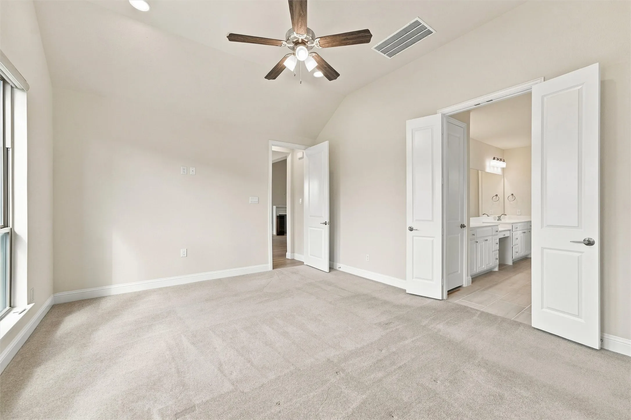 Vaulted ceiling with a central multi-blade ceiling fan, wall-to-wall carpeting, and double-door entry