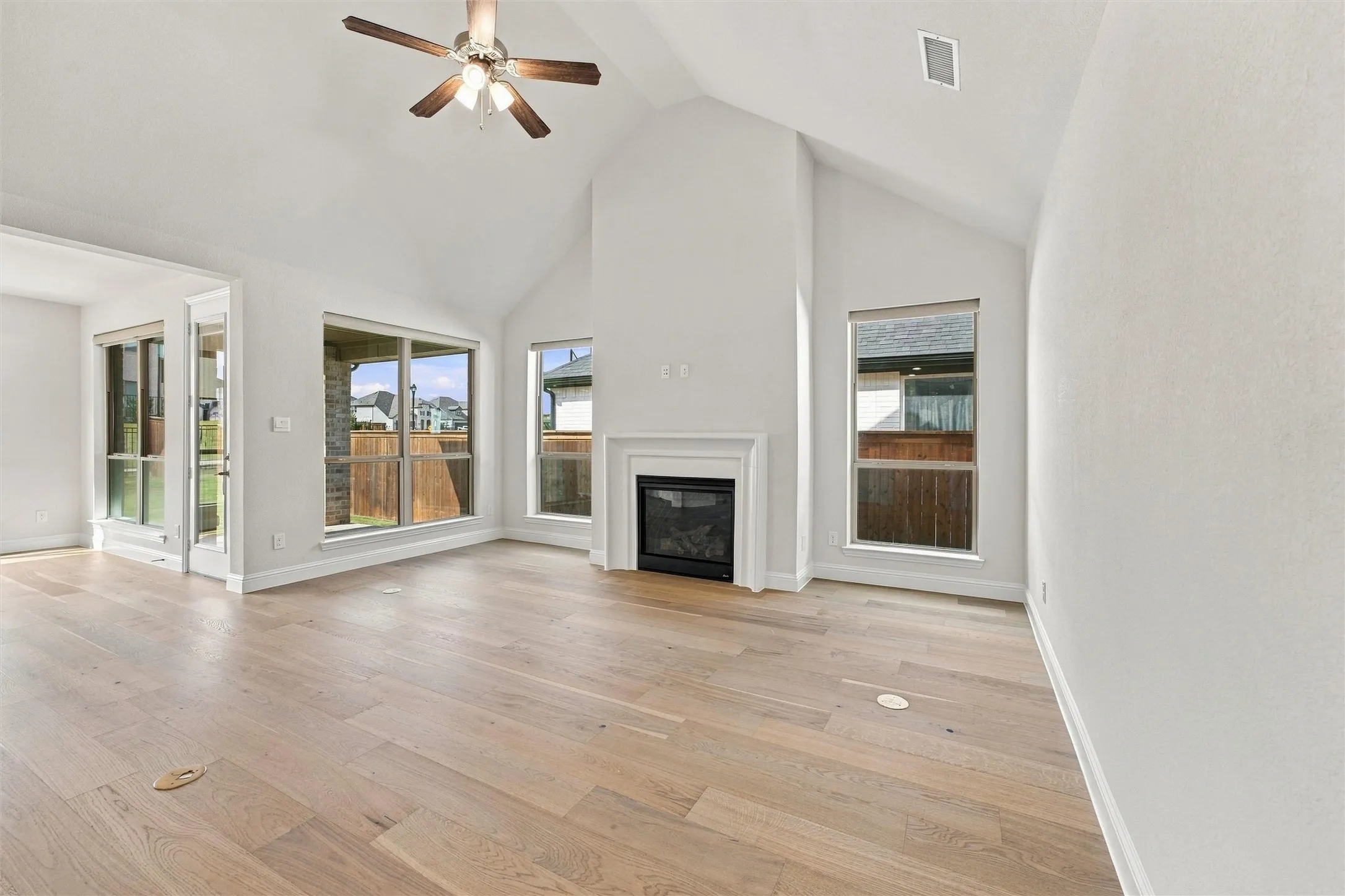 Vaulted ceilings, wood-finish flooring, central fireplace with a classic mantel, and large picture windows